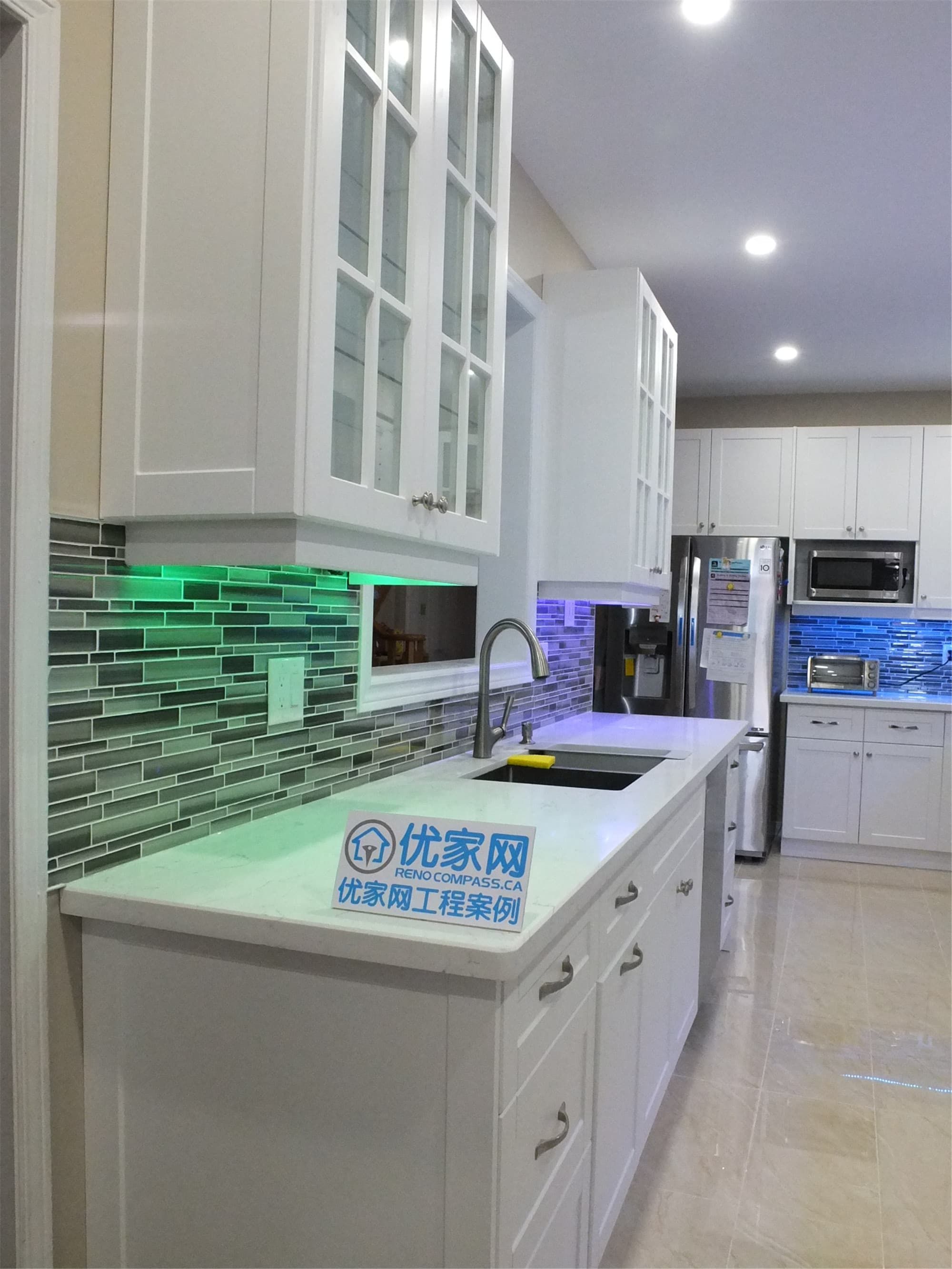 This Vaughan kitchen renovation highlights elegant white shaker cabinets with glass display doors, quartz countertops, and a modern glass mosaic backsplash enhanced by LED under-cabinet lighting. The clean layout and bright finishes create a stylish and functional cooking space. Completed by a trusted Toronto renovation company, the design blends modern aesthetics with everyday practicality.