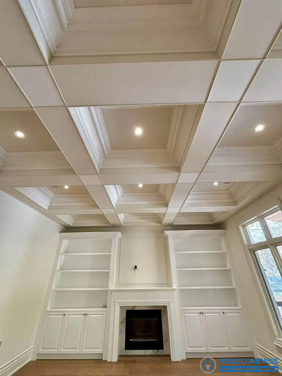 This image features a European-style living room defined by a coffered ceiling (waffle ceiling), symmetrical built-in shelving, and a centrally positioned fireplace. The coffered ceiling establishes clear structural rhythm and proportion, reinforcing the room’s architectural hierarchy. Full-height cabinetry and wall panelling frame the fireplace as a stable visual anchor, while integrated recessed lighting is carefully placed within the ceiling grid. This composition demonstrates disciplined spatial organization and refined craftsmanship within a high-end Richmond Hill interior renovation grounded in classical European architectural principles.