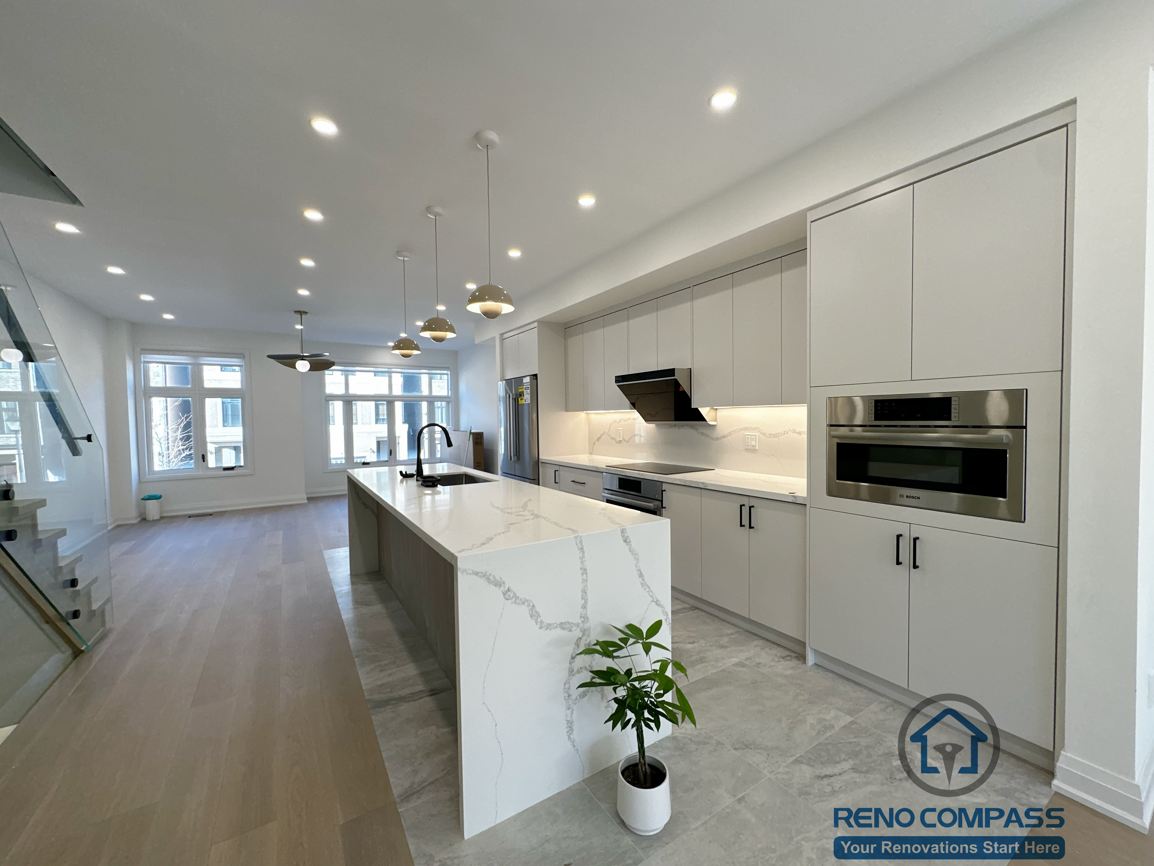 This Richmond Hill kitchen renovation showcases a modern open-concept layout with a full quartz waterfall island as the visual centerpiece. Custom flat-panel cabinetry, integrated appliances, and under-cabinet lighting create a clean, streamlined look, while warm wood flooring and layered pendant lighting add balance and depth to the space.