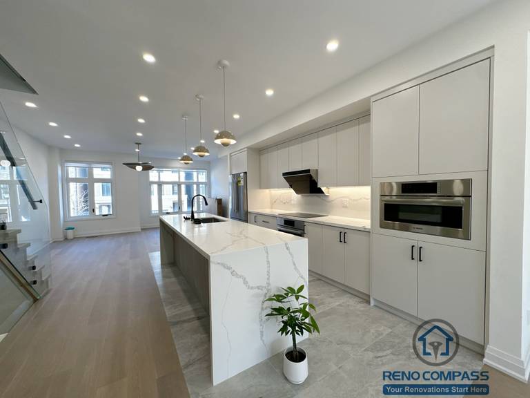 This Richmond Hill kitchen renovation showcases a modern open-concept layout with a full quartz waterfall island as the visual centerpiece. Custom flat-panel cabinetry, integrated appliances, and under-cabinet lighting create a clean, streamlined look, while warm wood flooring and layered pendant lighting add balance and depth to the space.