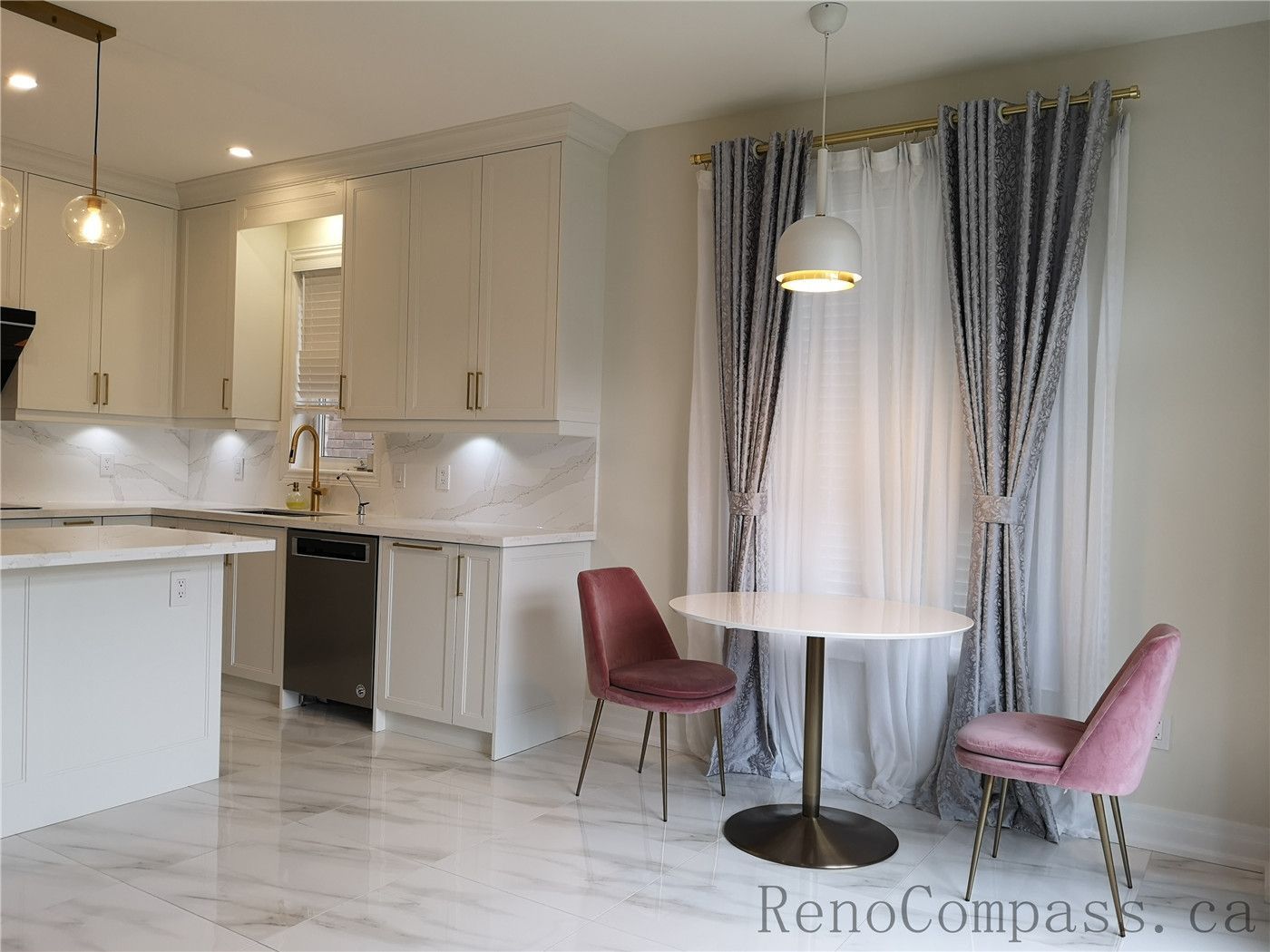 This Aurora interior renovation showcases a bright modern kitchen and dining area featuring custom white cabinetry, quartz countertops, marble-style flooring, and elegant gold hardware finishes. The open layout includes a cozy breakfast seating space with pendant lighting and full-height window drapery, creating a warm and inviting atmosphere. Completed by a professional Toronto renovation company focused on functional design, clean lines, and high-end finishing details.