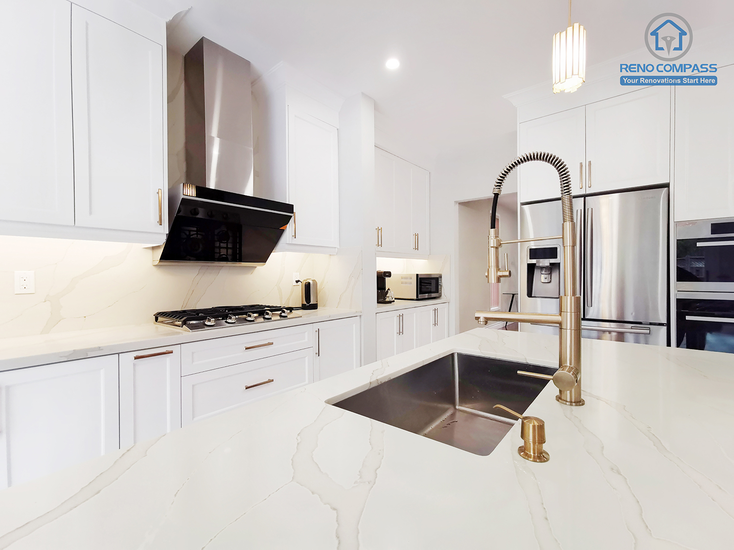 This Markham interior renovation highlights a custom kitchen island designed as a central functional workspace within the home. The oversized quartz countertop provides generous prep and serving space, while the integrated undermount sink and professional pull-down faucet enhance daily usability. White shaker cabinetry paired with warm metal hardware creates a balanced contrast between clean structure and subtle elegance. Built-in appliances and a streamlined range hood maintain visual clarity and efficient workflow across the kitchen. Completed by Reno Compass, this kitchen renovation reflects careful attention to proportion, material selection, and long-term practicality, tailored to modern Markham homeowners seeking refined yet highly functional interior design.