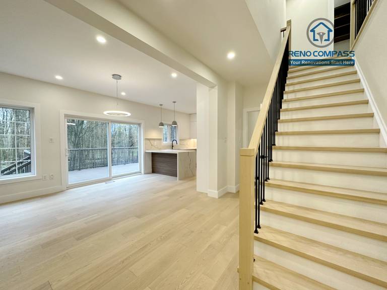 Open-concept main floor renovation in a Richmond Hill home featuring light-tone hardwood flooring, a modern staircase with wood treads and black railings, large windows for natural light, and a seamless connection to the kitchen and dining area.