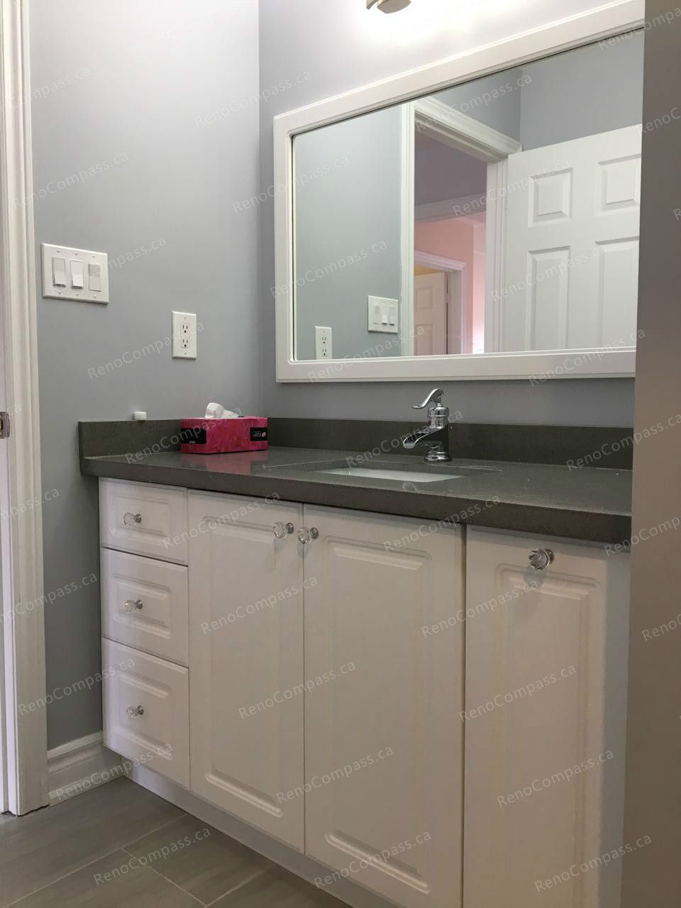 This Markham interior renovation showcases a clean and functional bathroom vanity upgrade with white cabinetry, a dark quartz countertop, and a large framed mirror. Soft grey wall tones and modern fixtures create a bright, contemporary atmosphere. Completed by a trusted Toronto renovation company, the renovation enhances daily functionality while delivering a refined and cohesive bathroom design.