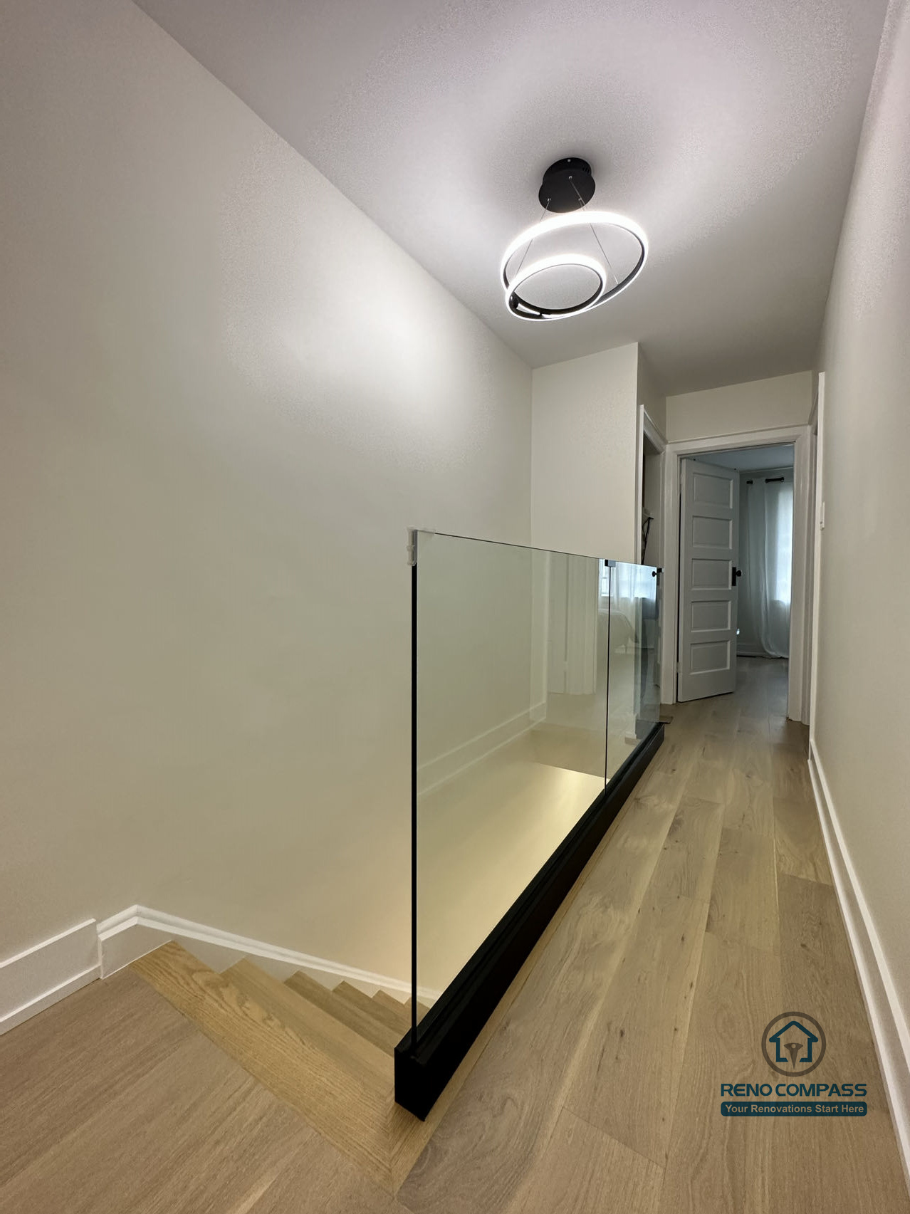 This Toronto interior renovation showcases an upper hallway with a sleek glass stair railing, wide-plank hardwood flooring, and modern ceiling lighting. The clean lines and safety-focused design enhance both openness and functionality, reflecting detailed craftsmanship by a professional Toronto renovation company.