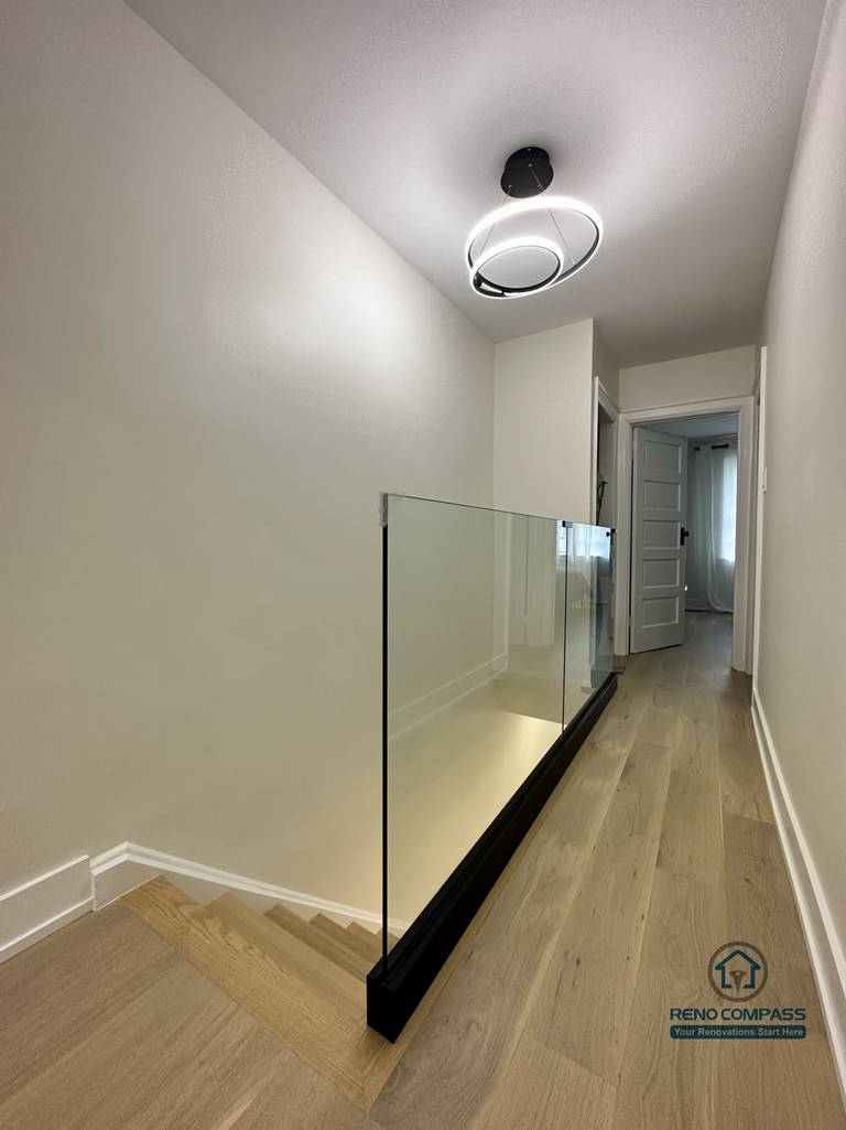 This Toronto interior renovation showcases an upper hallway with a sleek glass stair railing, wide-plank hardwood flooring, and modern ceiling lighting. The clean lines and safety-focused design enhance both openness and functionality, reflecting detailed craftsmanship by a professional Toronto renovation company.