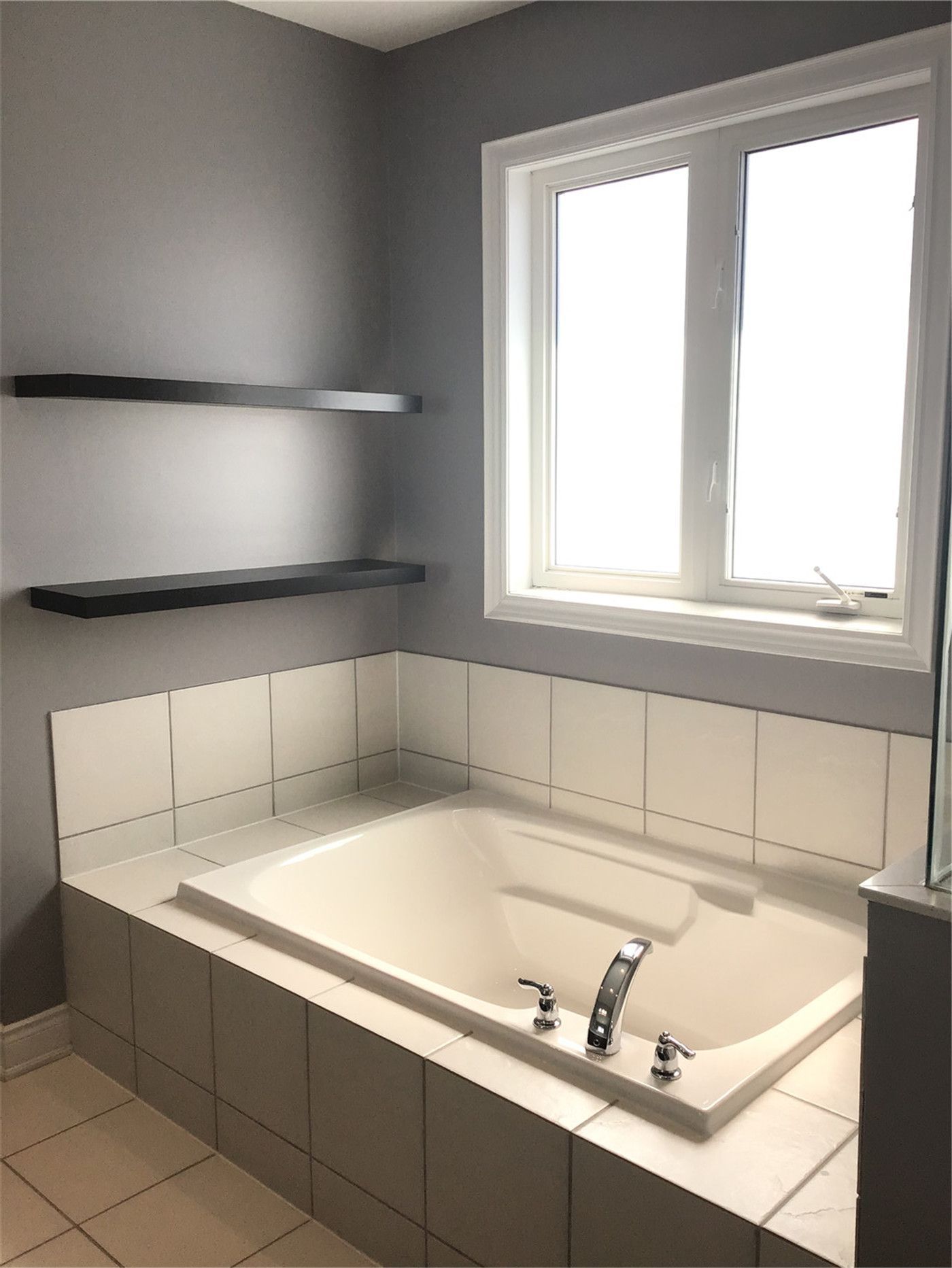 This Markham full home renovation features a clean and modern bathroom with a built-in soaking tub, tiled surround, and natural light from a large window. The minimalist design, neutral color palette, and functional shelving create a relaxing and spa-like atmosphere. Completed by a trusted Toronto Renovation Company, this space combines comfort with practical design.