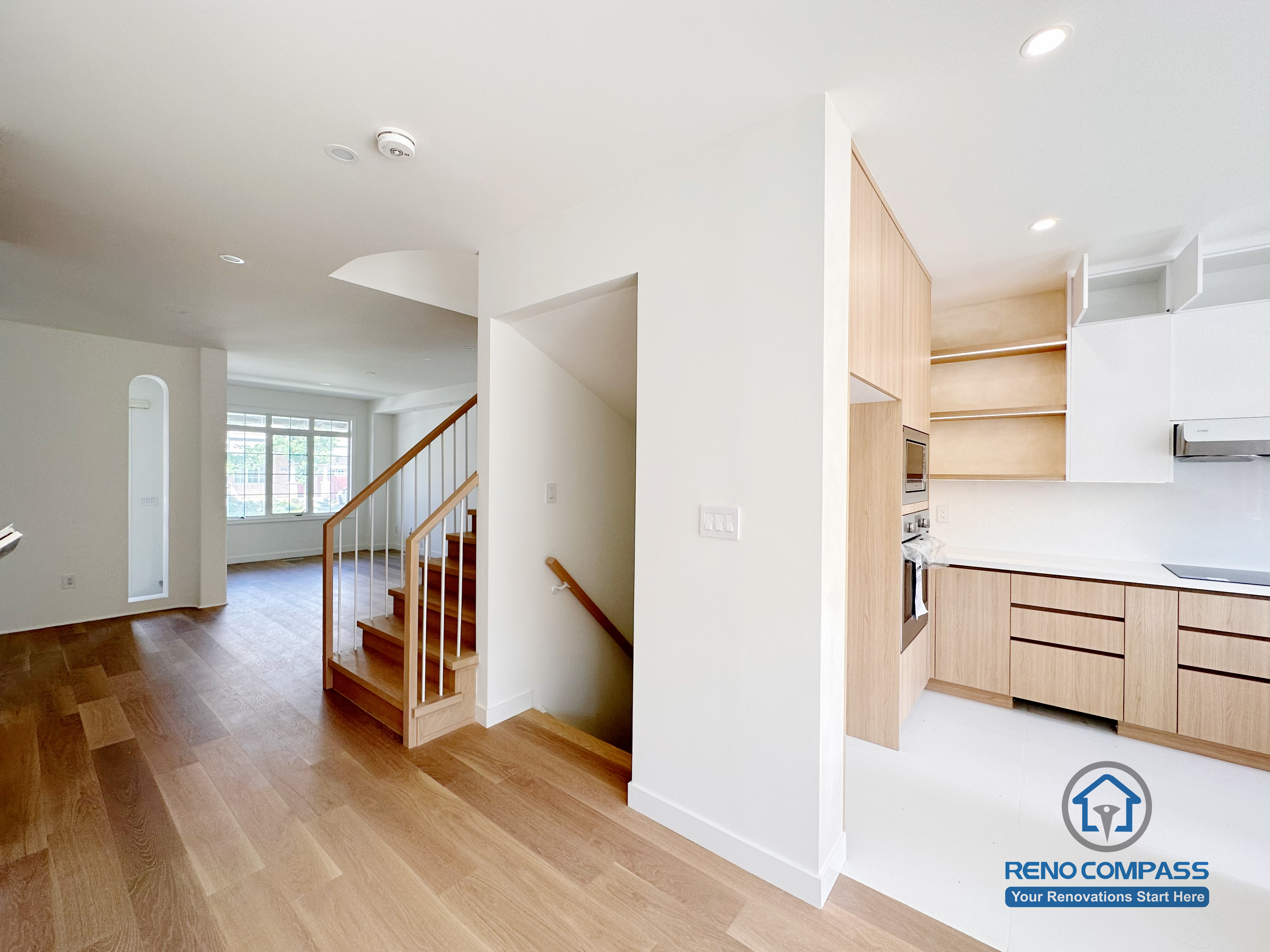 This image captures a Markham flooring and stair renovation highlighting the seamless transition between hardwood floors, the open staircase, and the adjacent kitchen area. Consistent wood tones, clean wall lines, and open sightlines create a cohesive layout that enhances flow and spatial clarity. Designed and completed by a trusted Toronto renovation company, Reno Compass Inc., this project emphasizes functional circulation, material consistency, and long-term residential performance.