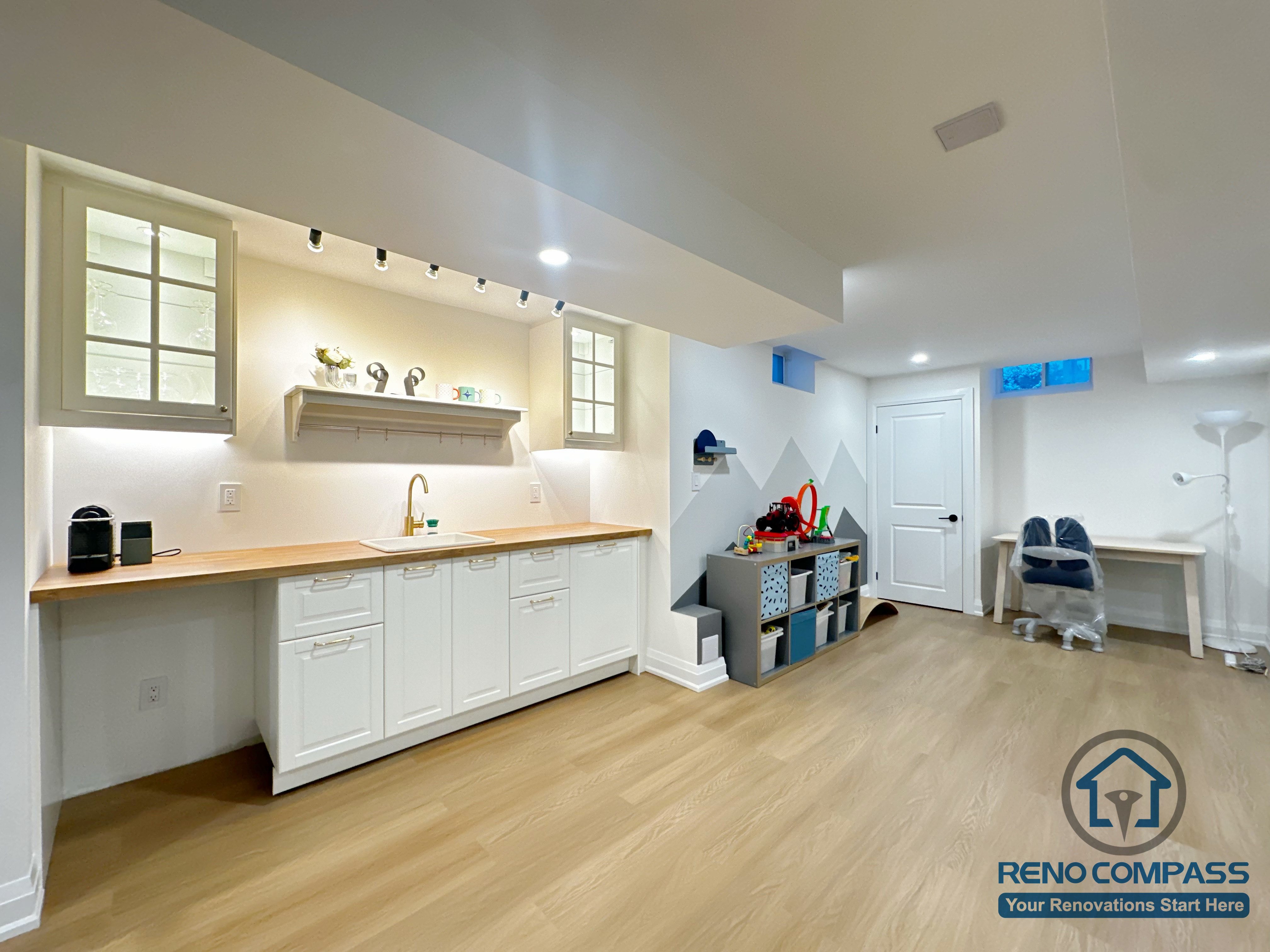 Basement renovation in Markham featuring a custom kitchenette with white cabinetry, wood countertop, under-cabinet lighting, and integrated sink. The design enhances everyday functionality while connecting seamlessly to a family-friendly activity and study area.