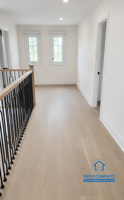 A bright second-floor landing featuring custom black metal railings, wide plank oak flooring, and abundant natural light during a luxury home renovation in Markham, Ontario. This modern hallway design enhances circulation, openness, and architectural elegance while connecting the home's private living spaces with premium craftsmanship by Reno Compass.