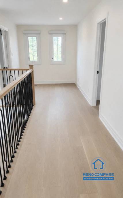 A bright second-floor landing featuring custom black metal railings, wide plank oak flooring, and abundant natural light during a luxury home renovation in Markham, Ontario. This modern hallway design enhances circulation, openness, and architectural elegance while connecting the home's private living spaces with premium craftsmanship by Reno Compass.