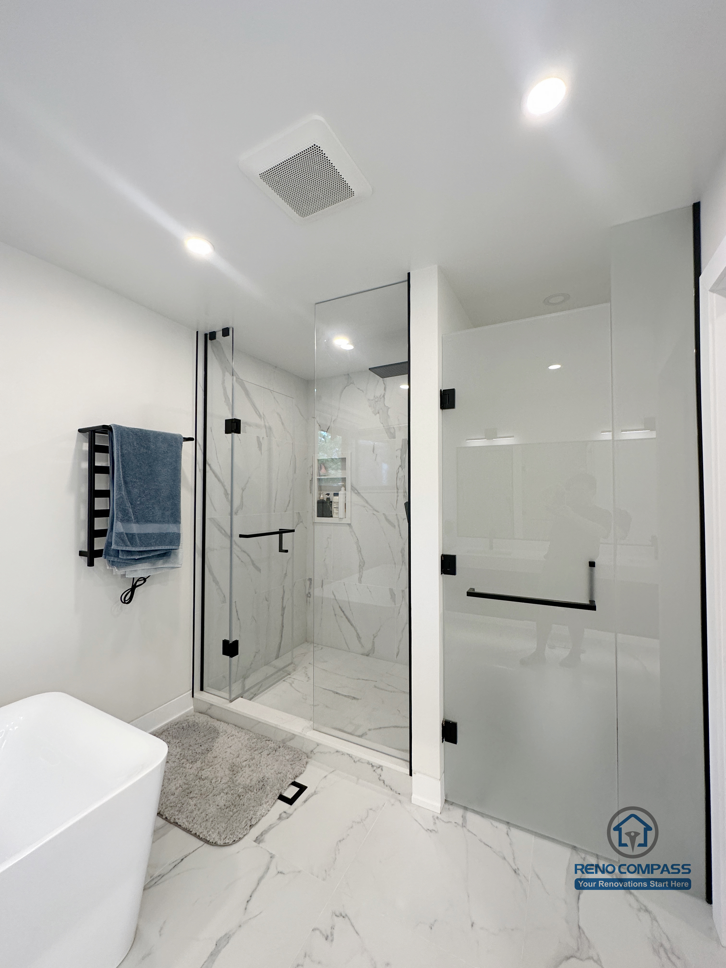 Modern bathroom renovation in Toronto featuring a frameless glass shower enclosure, marble-look porcelain tile walls and flooring, rainfall shower system, matte black hardware, and clean minimalist layout. Completed by a professional Toronto renovation company focused on durability, waterproofing, and modern comfort.