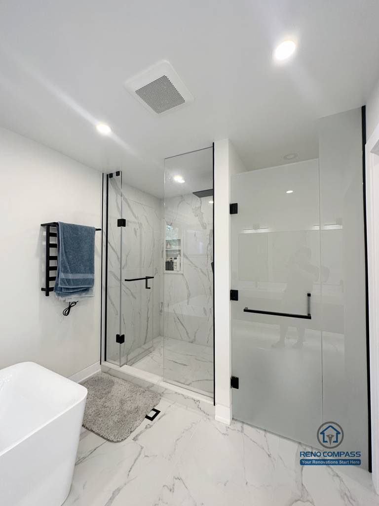Modern bathroom renovation in Toronto featuring a frameless glass shower enclosure, marble-look porcelain tile walls and flooring, rainfall shower system, matte black hardware, and clean minimalist layout. Completed by a professional Toronto renovation company focused on durability, waterproofing, and modern comfort.