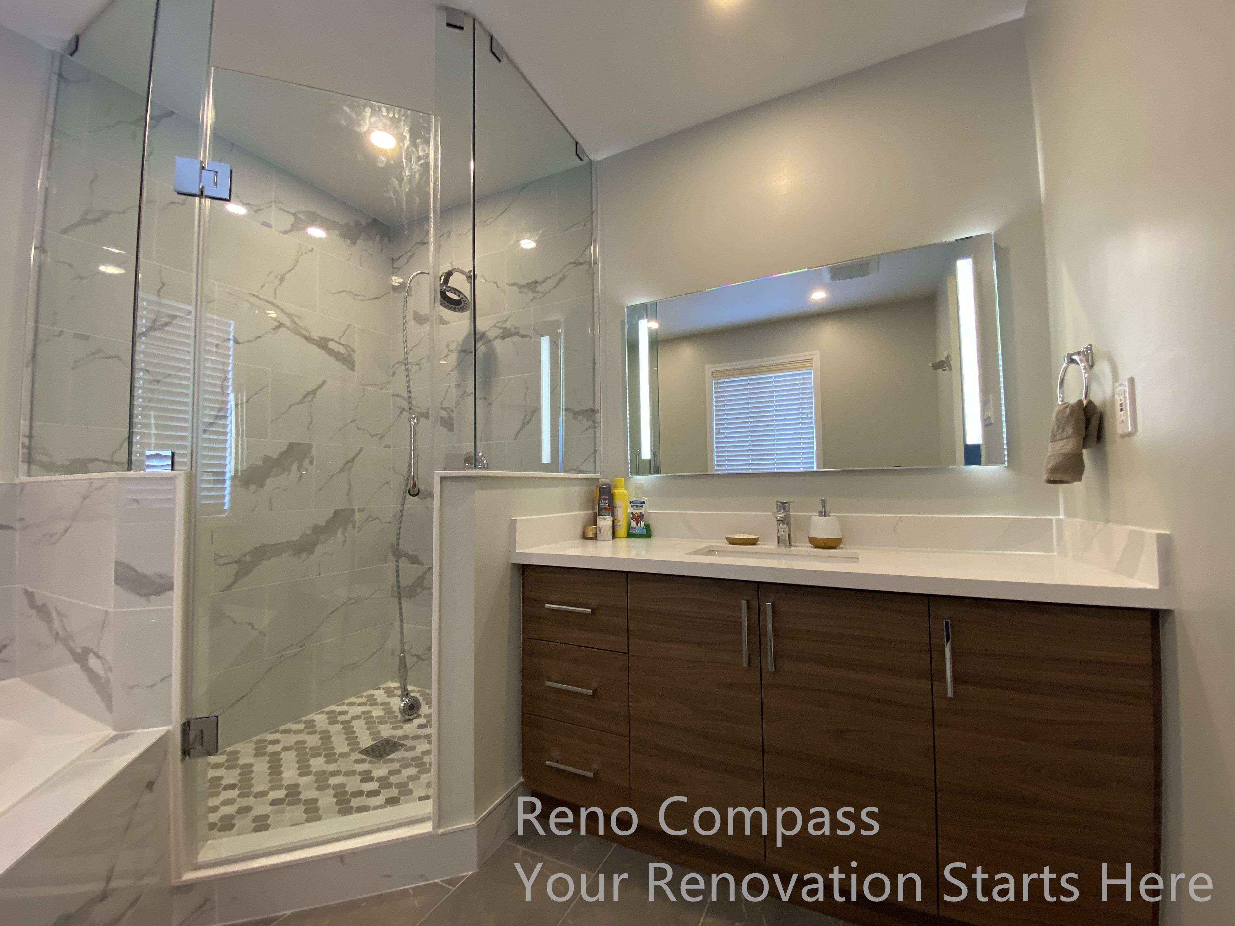 This Newmarket bathroom renovation showcases a modern vanity with ample storage paired with a frameless glass shower enclosure for a clean, contemporary look. The warm wood-tone cabinetry adds visual depth and contrast against the neutral wall finishes and marble-look shower tiles. An illuminated mirror enhances brightness and functionality, while the glass shower enclosure maintains openness and clear sightlines throughout the space. Carefully selected materials and streamlined fixtures create a balanced, spa-inspired bathroom that is both practical and easy to maintain. This renovation was completed by Reno Compass, serving homeowners in Newmarket and the surrounding GTA.