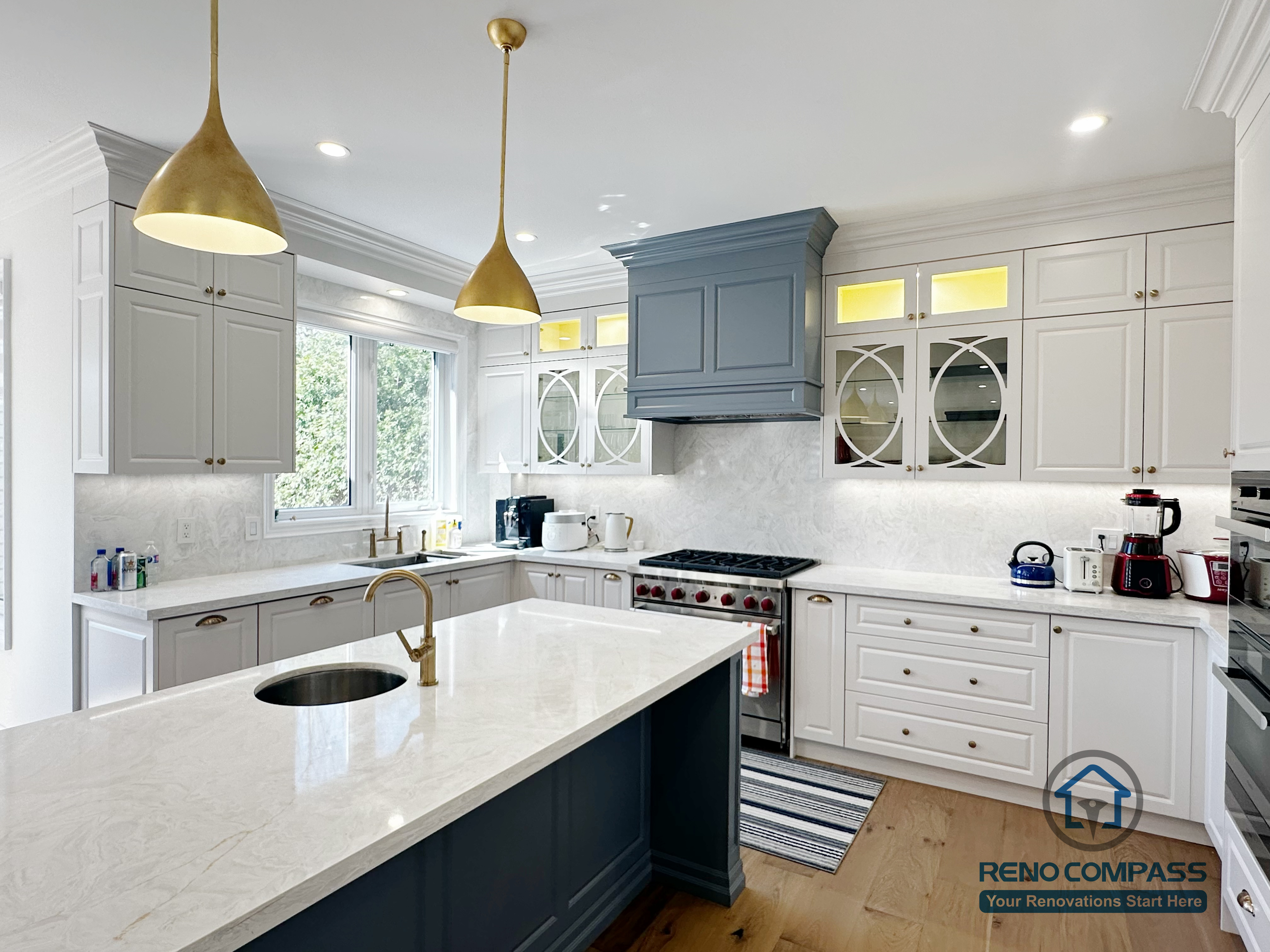 This North York kitchen renovation highlights a quartz waterfall island with an integrated sink, paired with warm brass pendant lighting and custom shaker cabinetry. The combination of functional workspace and layered lighting creates a bright, inviting kitchen designed for both daily use and entertaining, completed by Reno Compass.