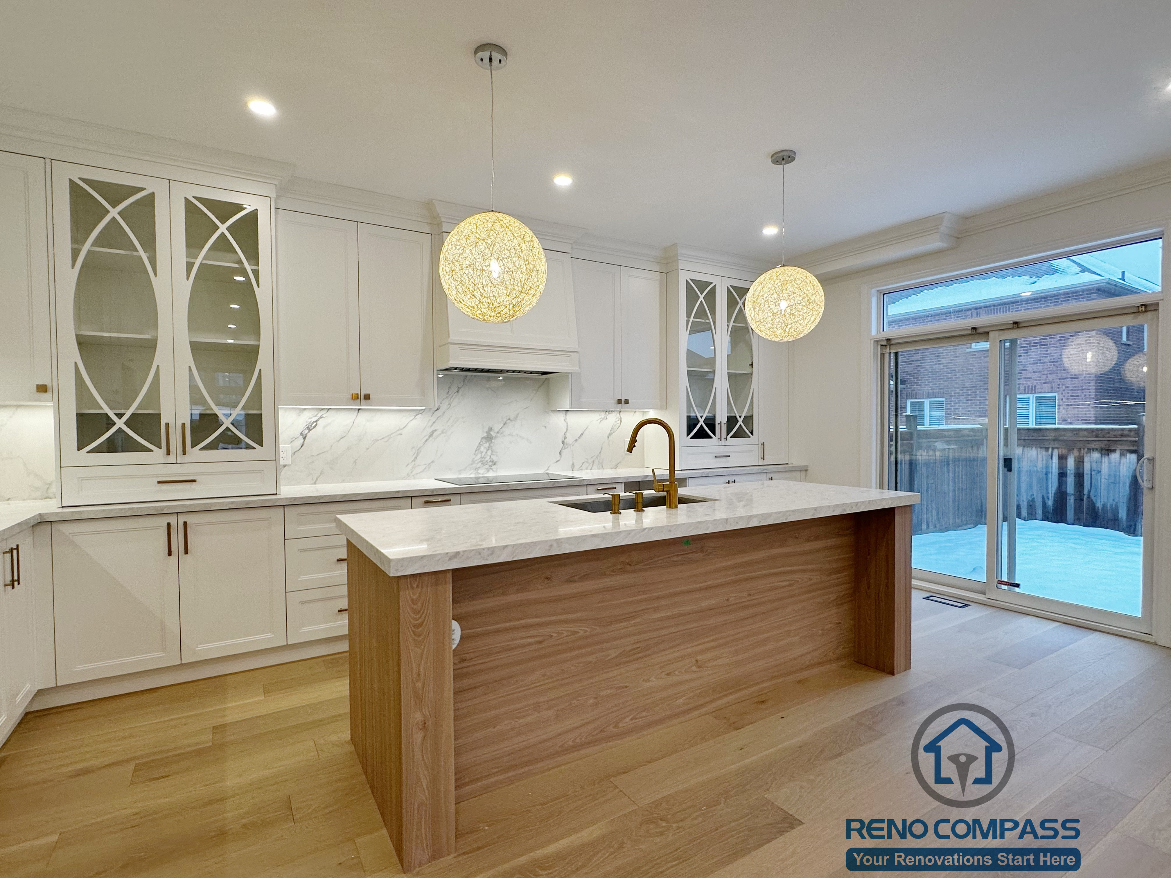 Custom white kitchen completed as part of a Vaughan interior renovation, featuring a large waterfall island with wood paneling, quartz countertops, marble-look backsplash, glass-front cabinets, built-in appliances, and modern pendant lighting. The clean layout and premium finishes highlight the craftsmanship of a professional Toronto renovation company.
