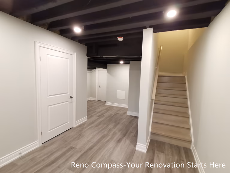This Vaughan basement renovation showcases a well-organized layout featuring an open staircase connection, dedicated functional zones, and an industrial-style sprayed black ceiling. Durable flooring, clean wall finishes, and recessed lighting create a cohesive and practical lower-level space. The design clearly separates circulation, storage, and activity areas while maintaining an open and uncluttered feel. Designed and completed by Reno Compass, this basement renovation emphasizes spatial efficiency, visual continuity, and long-term usability.