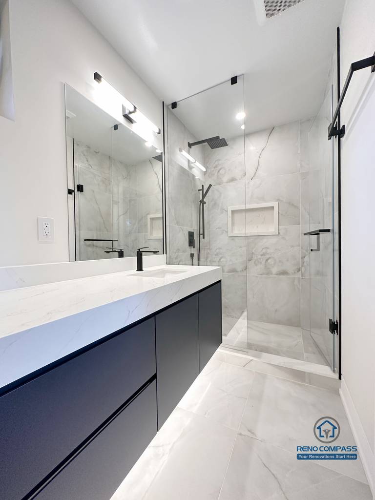 Modern bathroom renovation in Toronto showcasing a frameless glass walk-in shower, large-format marble-look tiles, floating custom vanity, and matte black fixtures. Completed by a professional Toronto renovation company with a focus on clean lines, durability, and contemporary design.