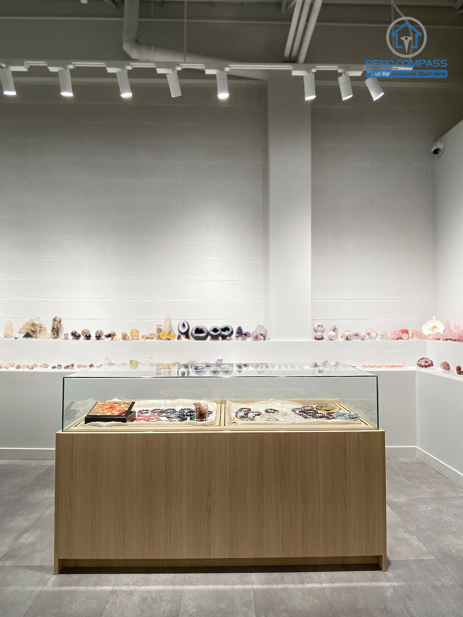 This image presents the central display area of a crystal shop renovation in Markham, featuring a custom-built wood and glass display island positioned along the main visual axis of the store. Wall-mounted crystal shelves, polished concrete flooring, and professional track lighting work together to create a clean, balanced, and gallery-like retail environment. The symmetrical layout enhances product visibility and customer flow. As a Toronto renovation company, Reno Compass specializes in retail renovations that combine thoughtful space planning with refined visual presentation.