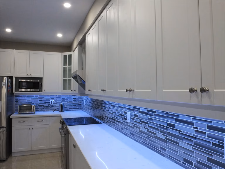 This Vaughan kitchen renovation showcases elegant white shaker cabinetry, quartz countertops, and a modern glass mosaic tile backsplash enhanced with soft LED under-cabinet lighting. The streamlined layout and bright finishes create a clean, contemporary cooking space. Completed by a professional Toronto renovation company, the design blends practical functionality with modern kitchen aesthetics.