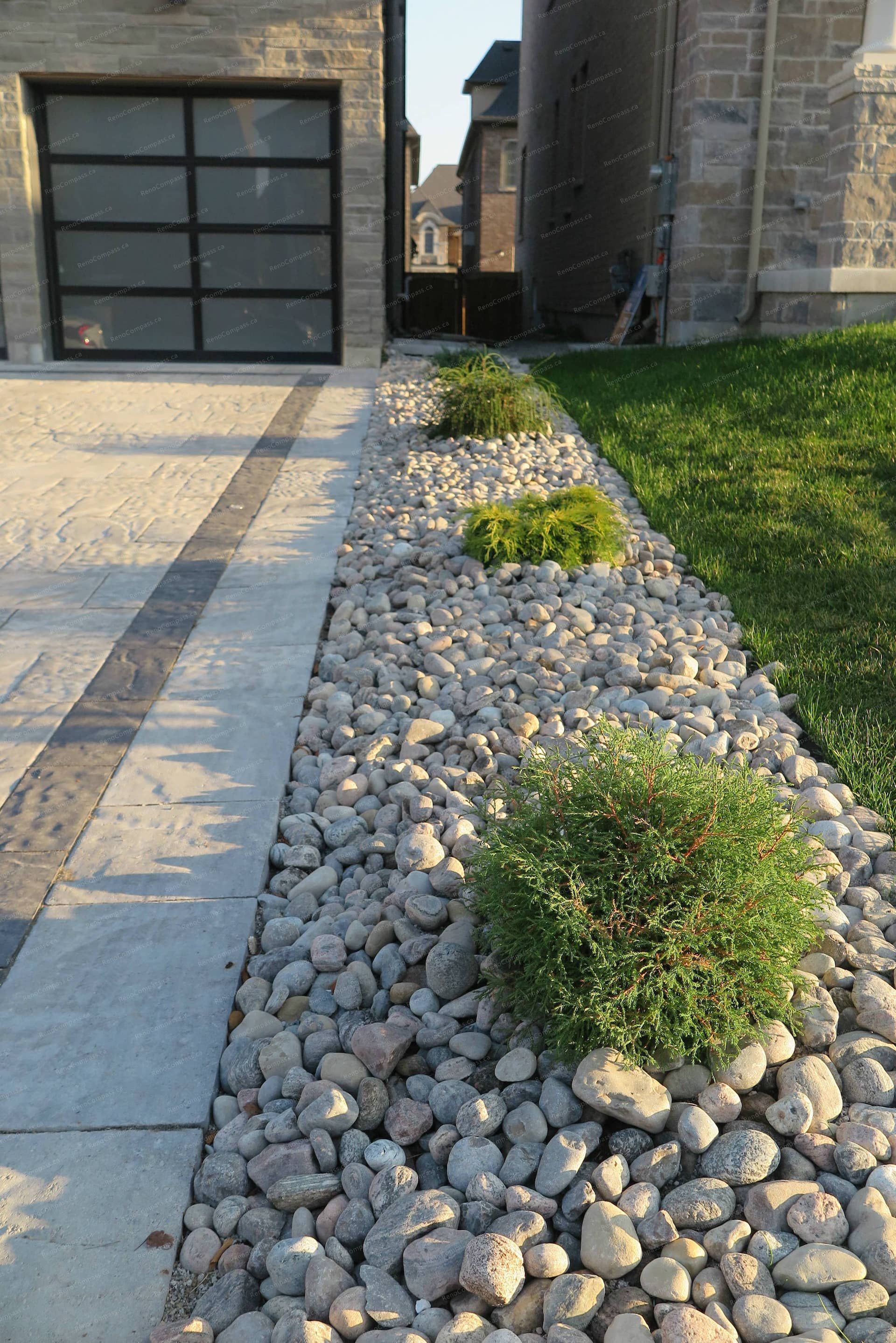 Front yard landscaping renovation in Vaughan featuring decorative river rock beds, modern driveway borders, and low-maintenance shrubs. This landscape design improves drainage, adds texture to the front yard, and creates a clean transition between the stamped concrete driveway and the lawn area, enhancing the home’s curb appeal.