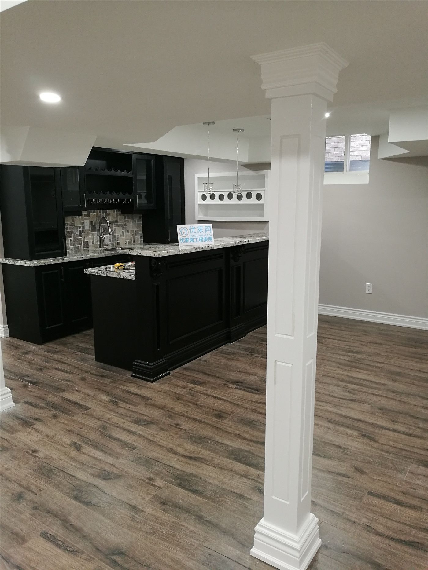This Richmond Hill basement renovation features a stylish modern home bar with dark cabinetry, a mosaic tile backsplash, and warm wood-look flooring. The elegant white column and custom bar design create a perfect entertainment space with contemporary finishes.