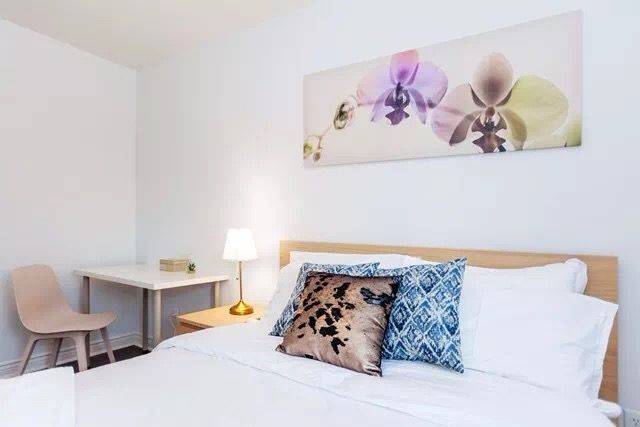 This Toronto interior renovation features a bright and cozy bedroom with clean white walls, minimalist furniture, and soft decorative accents. The space includes a comfortable bed, modern bedside lighting, and simple artwork that enhances the calm atmosphere. The renovation creates a relaxing and functional bedroom environment, perfect for comfortable living in a modern Toronto home.