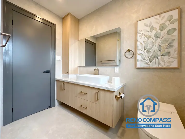 This contemporary powder room renovation features a floating vanity, warm wood cabinetry, premium brass fixtures, and a minimalist design aesthetic. The combination of soft textures, modern finishes, and smart storage solutions creates an elegant and functional space for everyday use. Project completed by Reno Compass, serving Markham, Toronto, Richmond Hill, Vaughan, and the Greater Toronto Area.