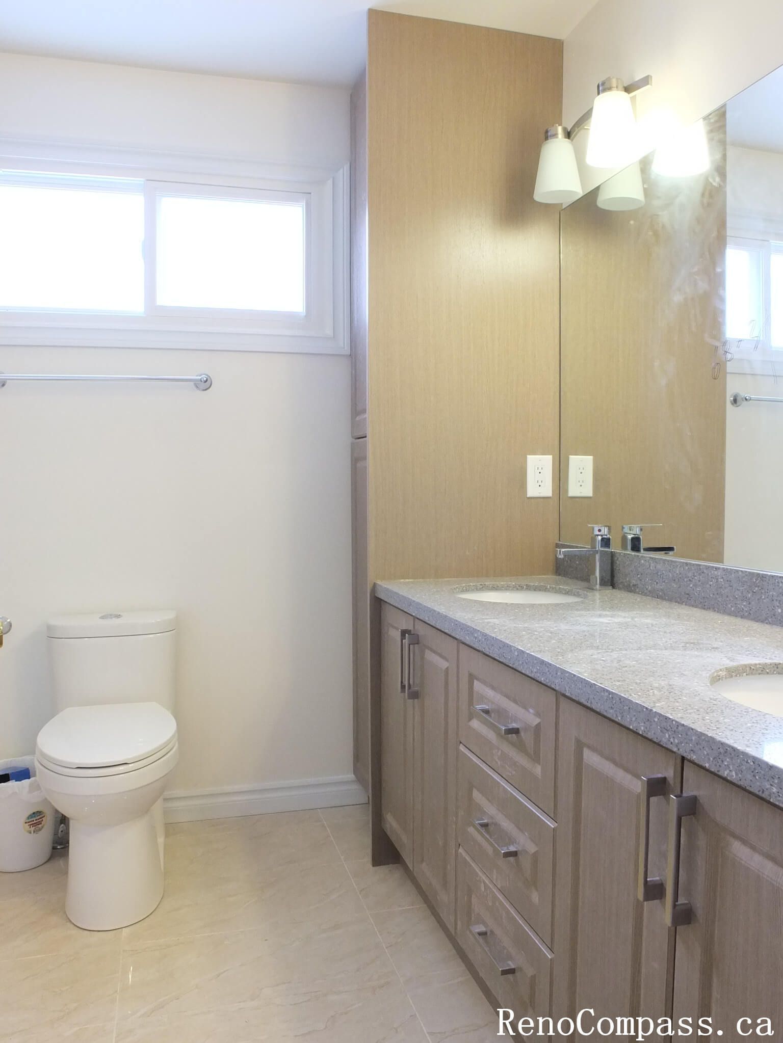 Bathroom renovation in North York showcasing a wood-tone vanity with integrated storage, quartz countertop, wall-mounted mirror, and modern lighting. This interior renovation highlights practical layout planning, neutral finishes, and long-term durability for Toronto residential homes.