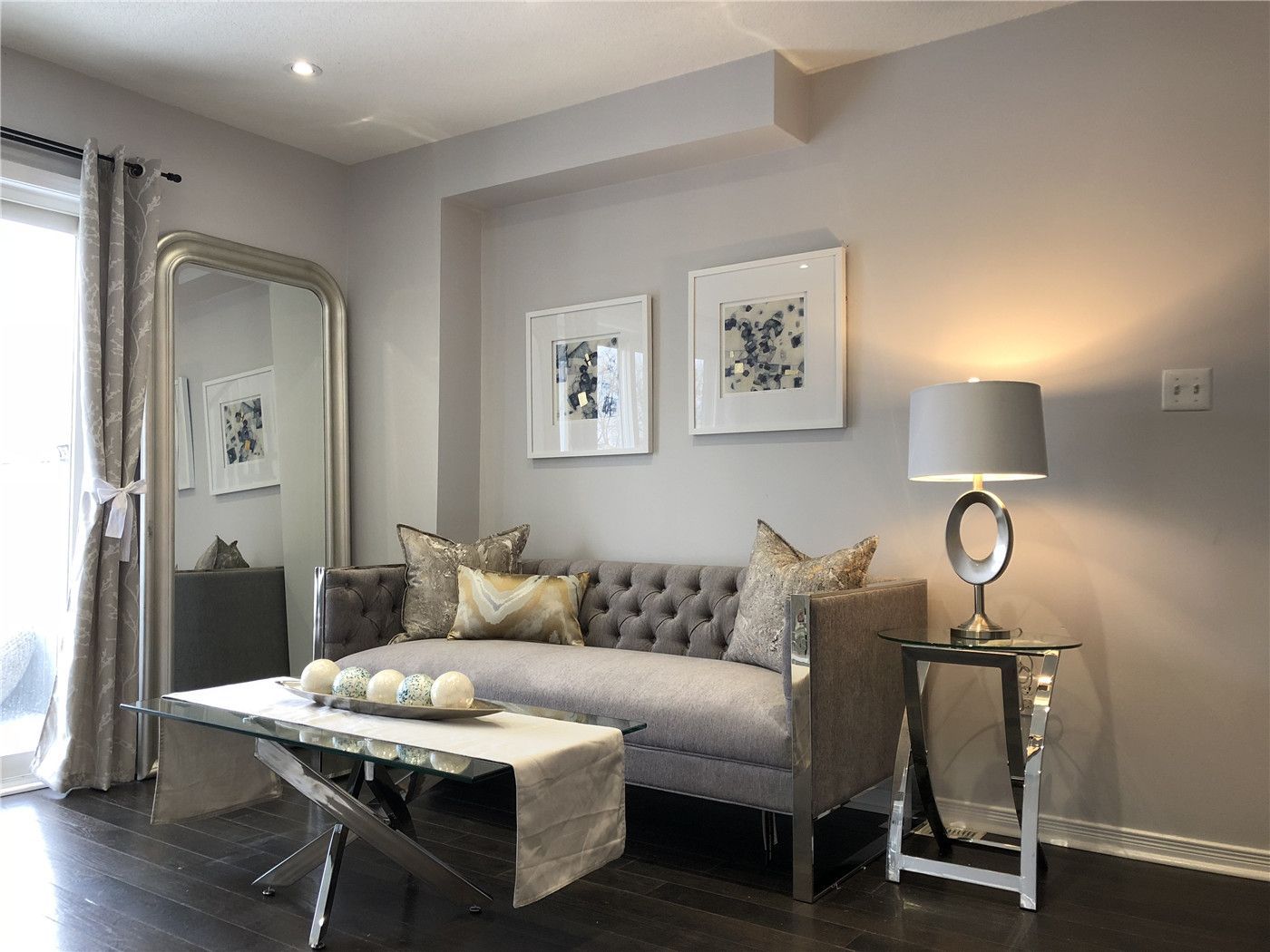 This Toronto interior design pre-sale staging features a cozy and elegant sitting area with a tufted sofa, mirrored accent piece, and modern glass coffee table. Soft lighting, neutral color tones, and carefully selected décor create a welcoming and sophisticated ambiance.