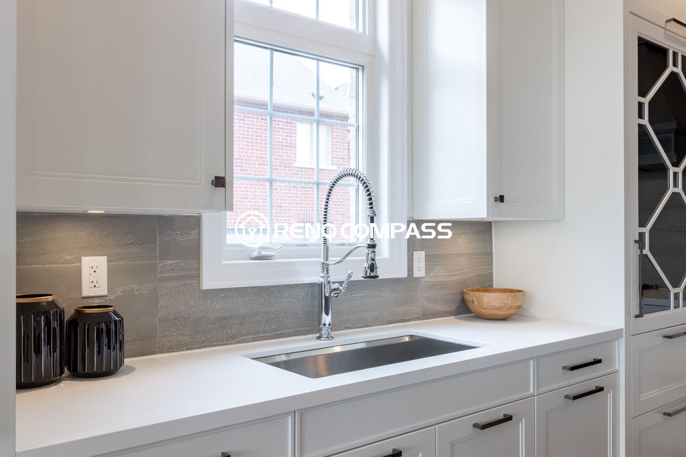 This Newmarket kitchen renovation highlights a clean sink and countertop area with a stainless steel faucet, quartz countertop, and modern backsplash tiles. The window above the sink brings natural light into the space, enhancing the bright and contemporary kitchen design. Completed by a professional Toronto renovation company, Reno Compass Inc., the project demonstrates attention to detail and high-quality finishing.