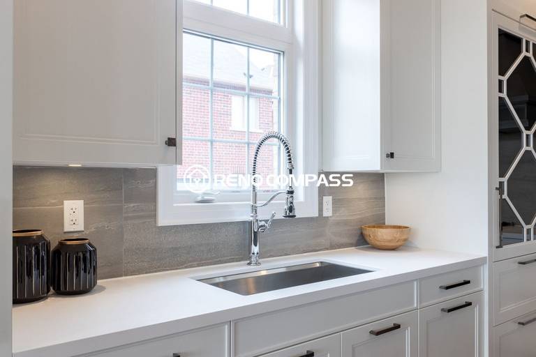 This Newmarket kitchen renovation highlights a clean sink and countertop area with a stainless steel faucet, quartz countertop, and modern backsplash tiles. The window above the sink brings natural light into the space, enhancing the bright and contemporary kitchen design. Completed by a professional Toronto renovation company, Reno Compass Inc., the project demonstrates attention to detail and high-quality finishing.