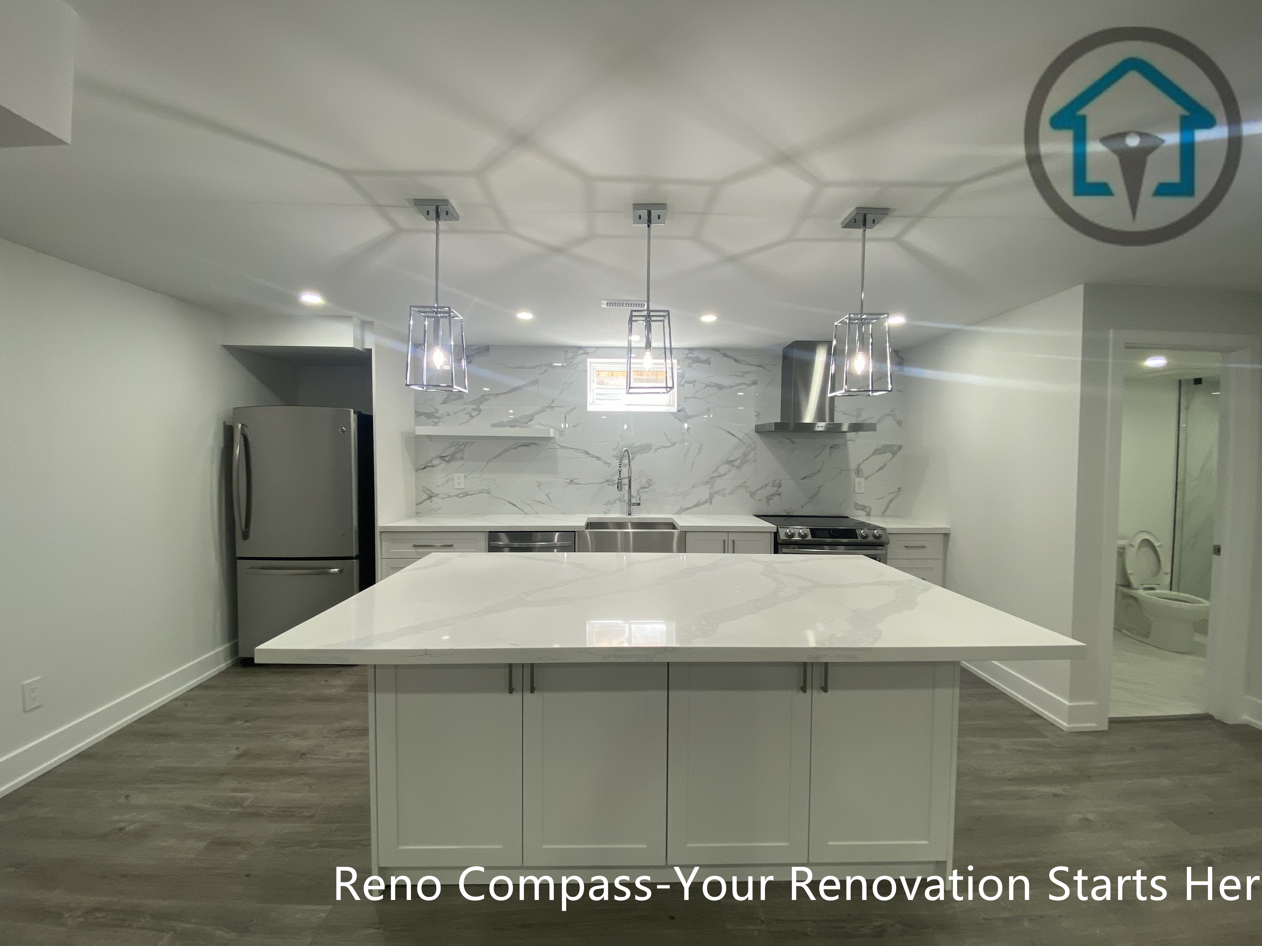 This image features a modern basement kitchen renovation in Newmarket completed by an experienced Toronto renovation company. The design centers around a large quartz island with shaker-style cabinetry, complemented by stainless steel appliances, marble-look backsplash, and contemporary pendant lighting. Recessed ceiling lights and neutral finishes enhance brightness and functionality, making the basement kitchen ideal for daily use, entertaining, or rental purposes.