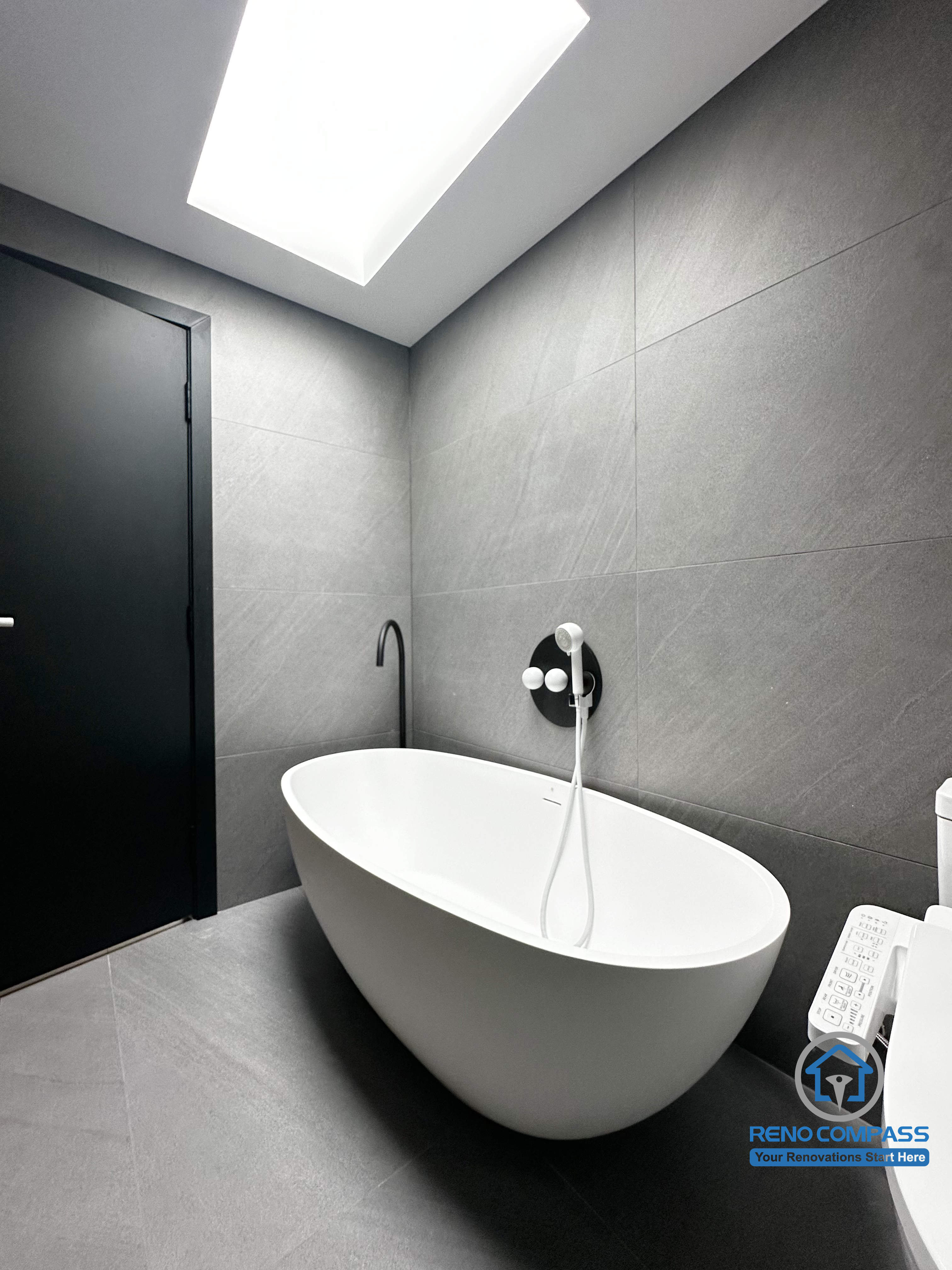 This image highlights the freestanding bathtub area in a Richmond Hill bathroom renovation. Clean architectural lines, large-format grey tiles, and a minimalist wall-mounted faucet create a calm, spa-like atmosphere. Natural light from the skylight enhances the sense of openness, while the matte black door adds contrast and depth. Designed and completed by Reno Compass, this space reflects a modern, refined bathroom renovation in the Greater Toronto Area.