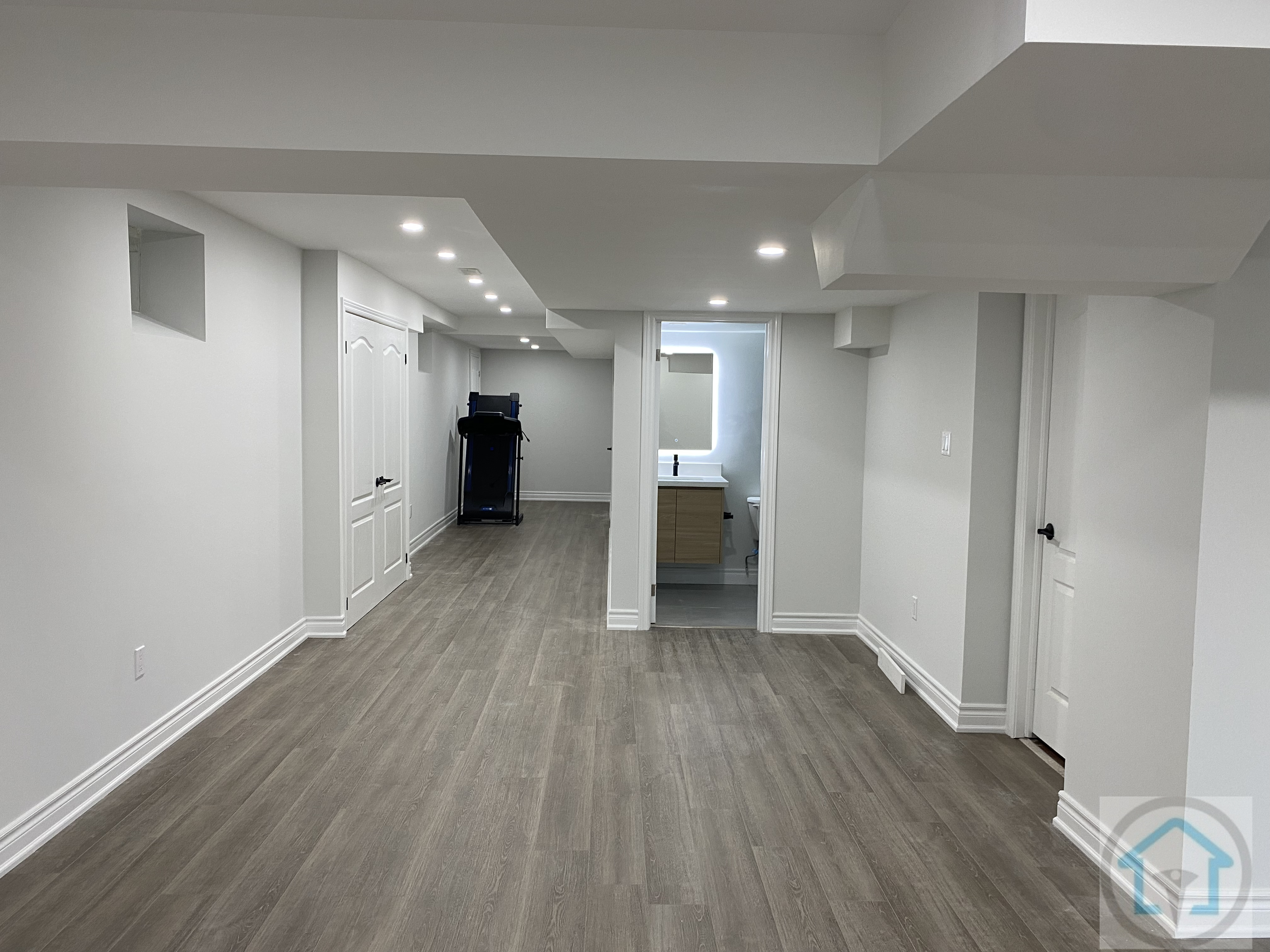 This Aurora basement renovation features an open-concept layout with modern flooring, bright recessed lighting, and clean white walls. The design maximizes natural light and creates a versatile living space suitable for family activities or entertainment. Contractor: Reno Compass Inc., City: Aurora.