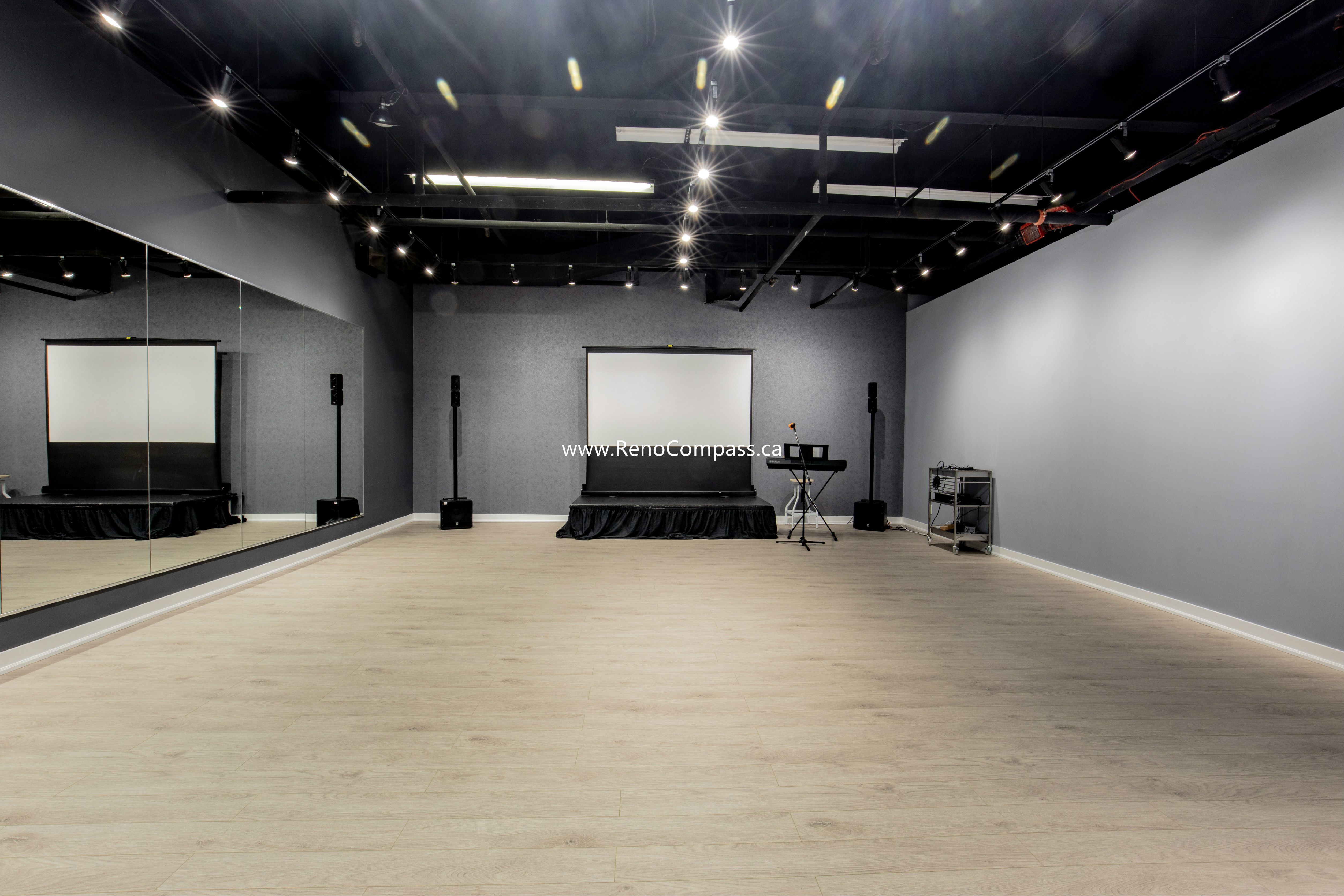 A spacious commercial studio renovation featuring luxury vinyl plank flooring, full-length mirrors, and professional track lighting. This Richmond Hill project showcases a modern industrial aesthetic with an exposed black ceiling, perfect for music schools and dance studios.