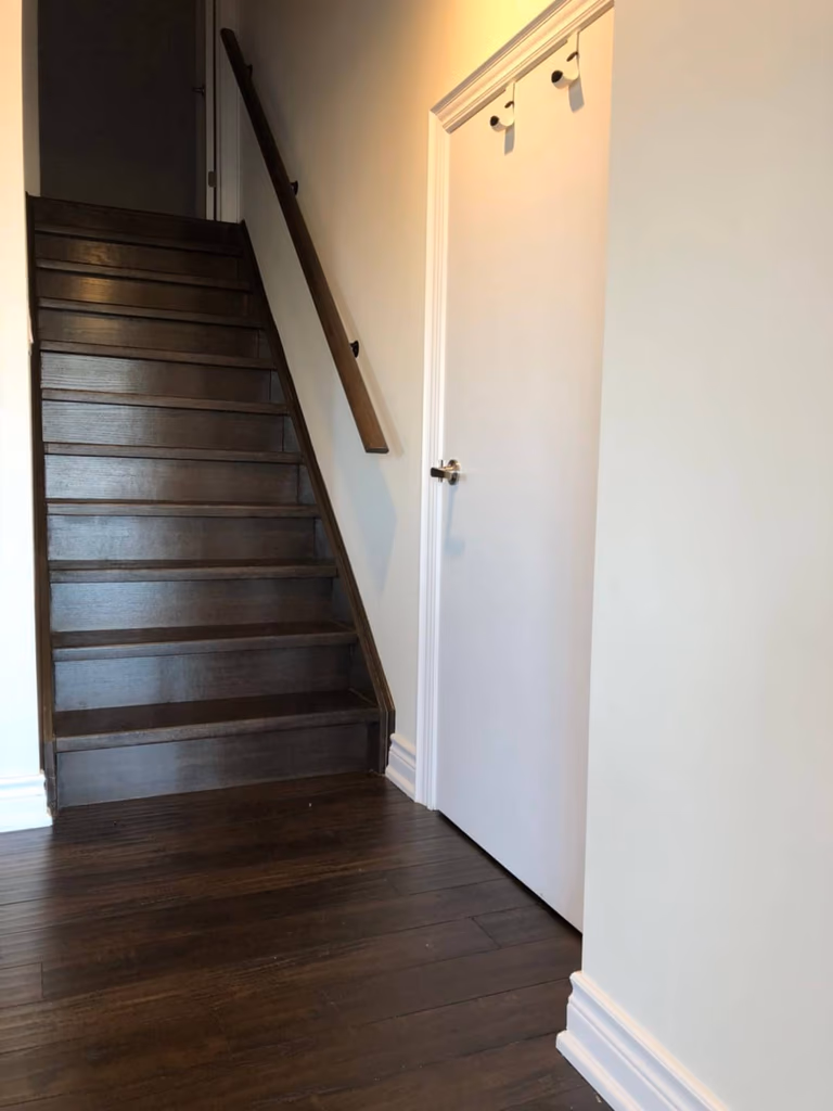 Newly finished hardwood staircase completed as part of a Toronto basement renovation, featuring dark-stained wood treads, matching flooring transition, clean white trim, and modern handrail installation for a seamless connection between levels.