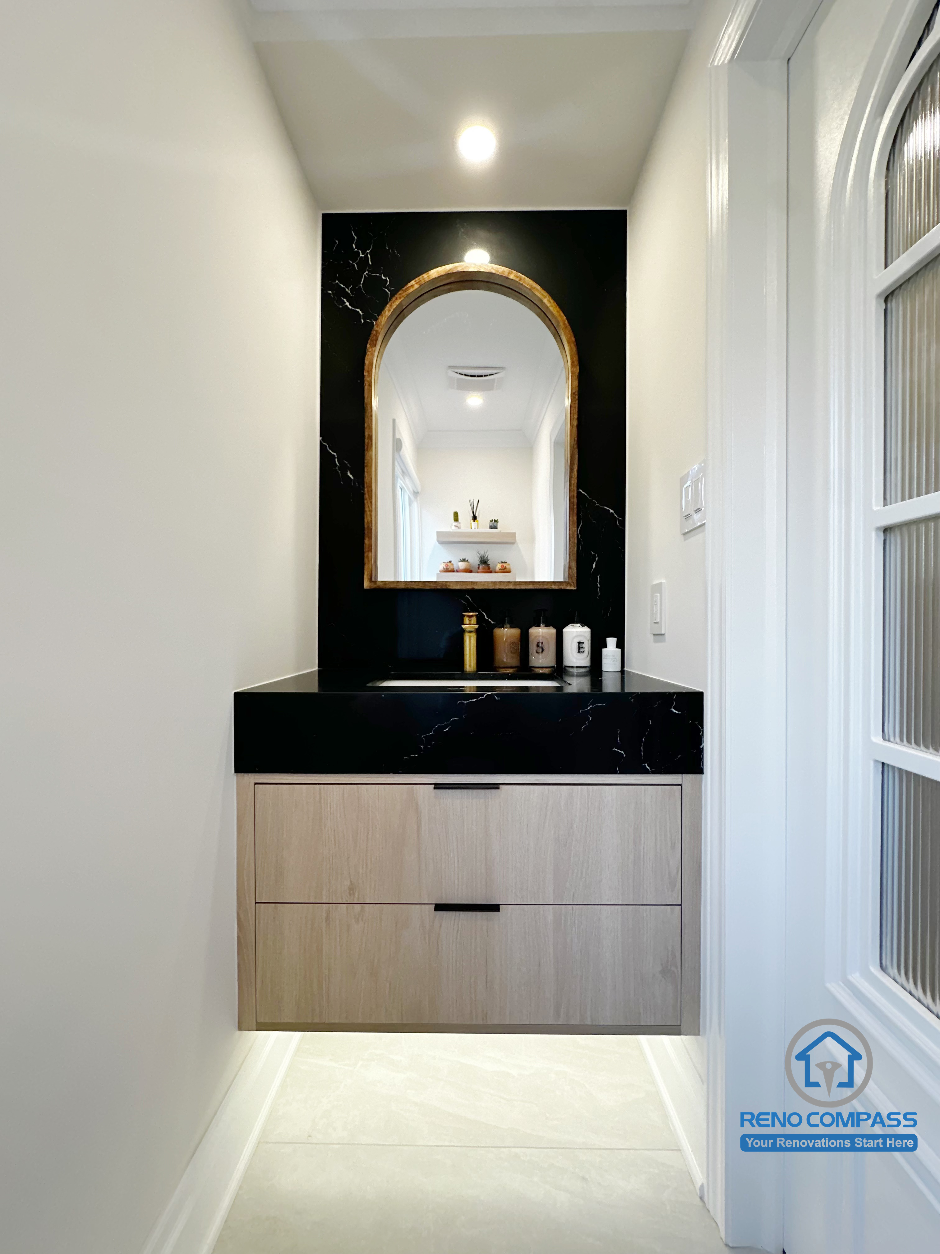 This image highlights a compact vanity area within the Markham bathroom renovation, designed as a visual pause between circulation and bathing zones. A floating wood vanity is paired with a black stone feature wall and an arched mirror, creating a strong focal point without overwhelming the narrow space. Integrated lighting and clean lines keep the area refined and intentional, demonstrating how secondary vanity zones can remain functional while contributing to the overall design language of the bathroom.