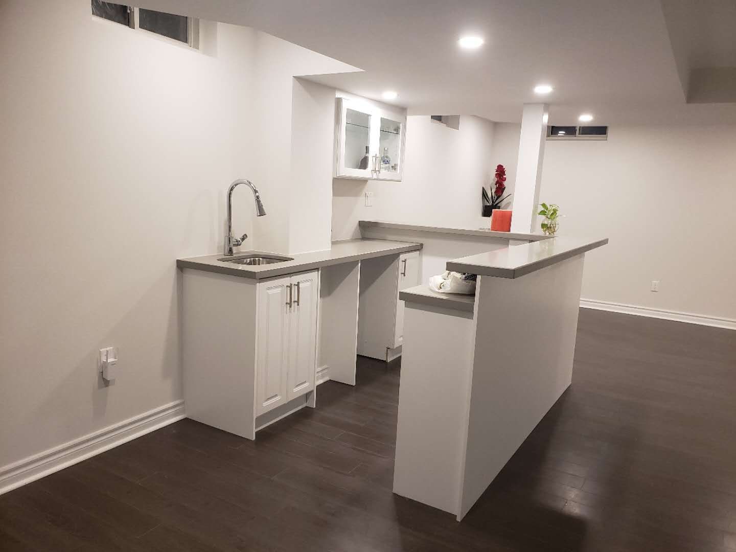 This Markham basement renovation features a clean and modern bar area with custom white cabinetry, a built-in sink, and a functional island countertop. Recessed pot lights and smooth ceiling finishes enhance brightness, while dark flooring adds contrast and warmth. The layout is designed to maximize usability and flow, making the basement ideal for entertaining, family gatherings, or multi-purpose living. This project reflects professional basement renovation standards in Markham, focusing on durability, lighting, and practical space planning.
