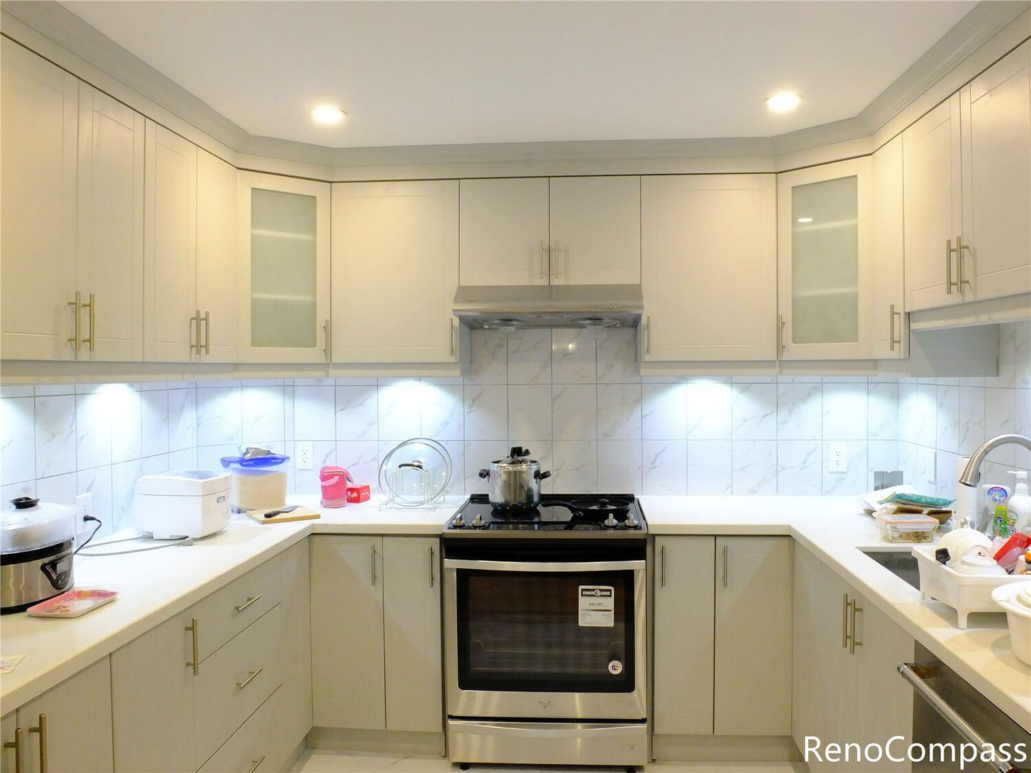 This Aurora kitchen renovation features elegant custom white cabinetry with gold hardware, a marble-style backsplash, and modern recessed lighting. The upgraded layout improves functionality while creating a bright and sophisticated cooking space. Completed with clean countertop finishes and integrated under-cabinet lighting, this renovation reflects the quality craftsmanship and attention to detail delivered by Reno Compass Inc., a trusted Toronto renovation company serving Aurora and the Greater Toronto Area.