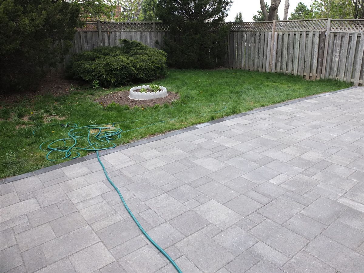 A completed backyard interlocking patio installation in Mississauga featuring large-format grey stone pavers, clean edge borders, and a modern low-maintenance outdoor design. This landscaping renovation improves outdoor usability and creates a durable patio space ideal for relaxation and gatherings. Completed by a professional Toronto Renovation Company, Reno Compass Inc., specializing in interlocking, landscaping, and exterior home upgrades across the GTA.