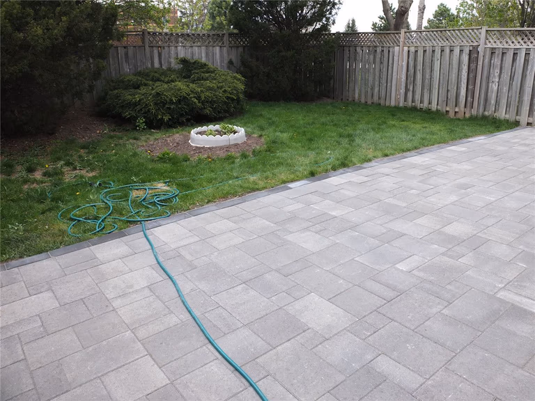 A completed backyard interlocking patio installation in Mississauga featuring large-format grey stone pavers, clean edge borders, and a modern low-maintenance outdoor design. This landscaping renovation improves outdoor usability and creates a durable patio space ideal for relaxation and gatherings. Completed by a professional Toronto Renovation Company, Reno Compass Inc., specializing in interlocking, landscaping, and exterior home upgrades across the GTA.