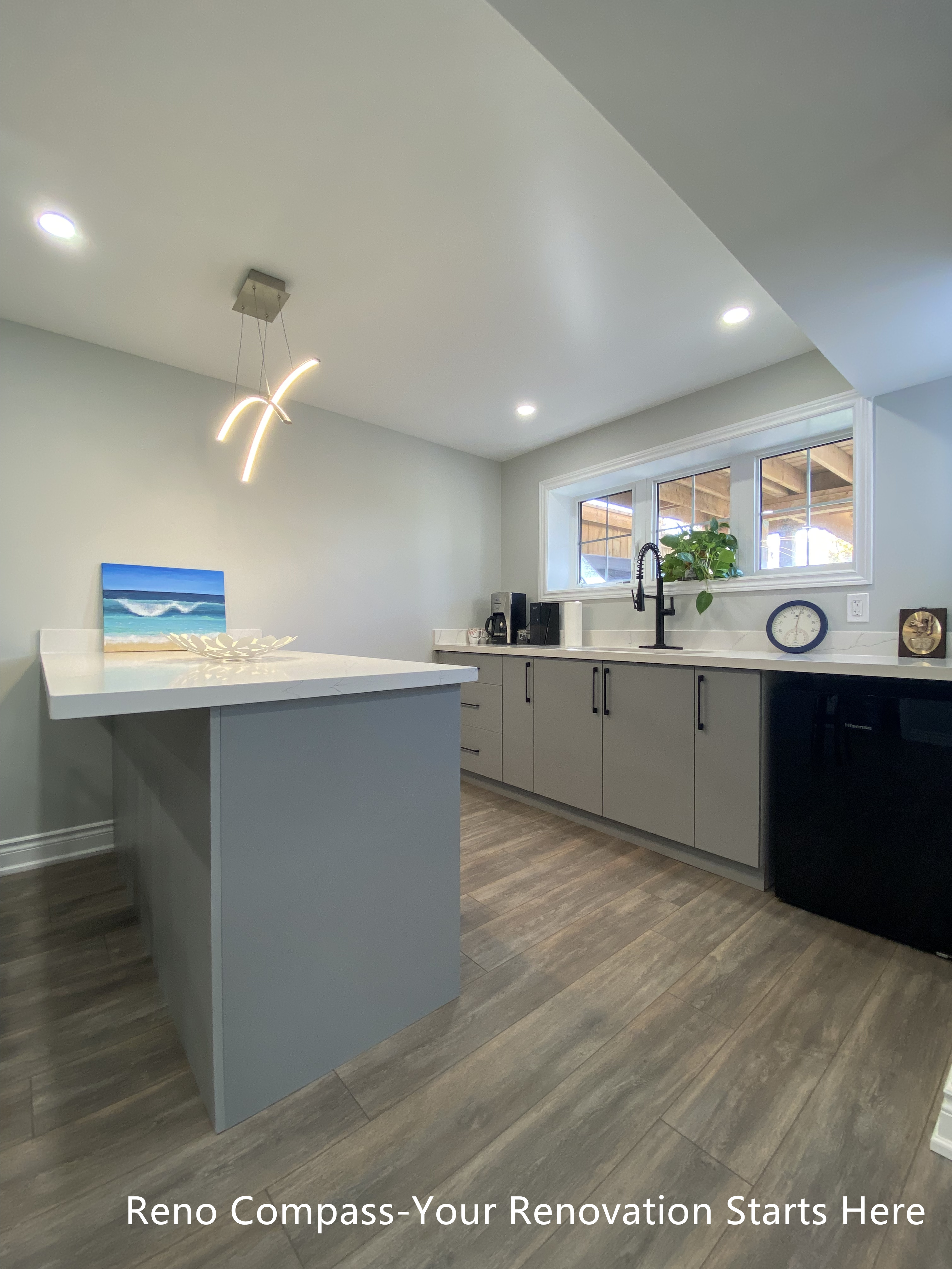 Modern basement bar renovation in Oakville featuring a large quartz island countertop, custom base cabinets, contemporary pendant lighting, vinyl plank flooring, and a compact kitchenette layout designed for entertaining and everyday use, completed by Reno Compass Inc.