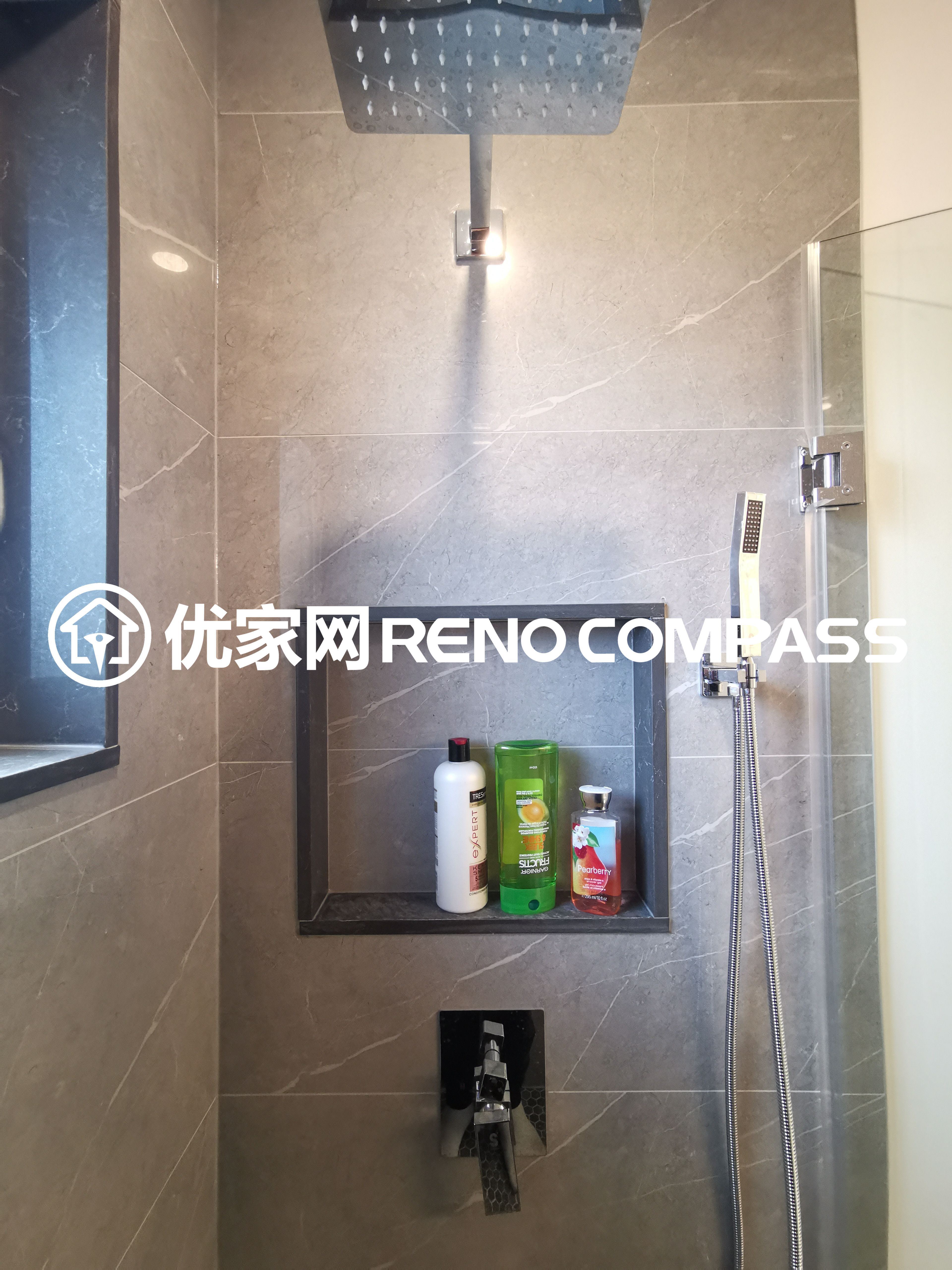 This image highlights a detailed view of a walk-in shower completed as part of a North York interior renovation project. The shower features a ceiling-mounted rain shower head, a handheld shower system, and a built-in wall niche for convenient storage. Large-format wall tiles create a clean and cohesive look, while the recessed niche adds both functionality and visual depth. The modern fixture layout and precise tile installation demonstrate quality craftsmanship and thoughtful bathroom design tailored for contemporary Toronto homes.
