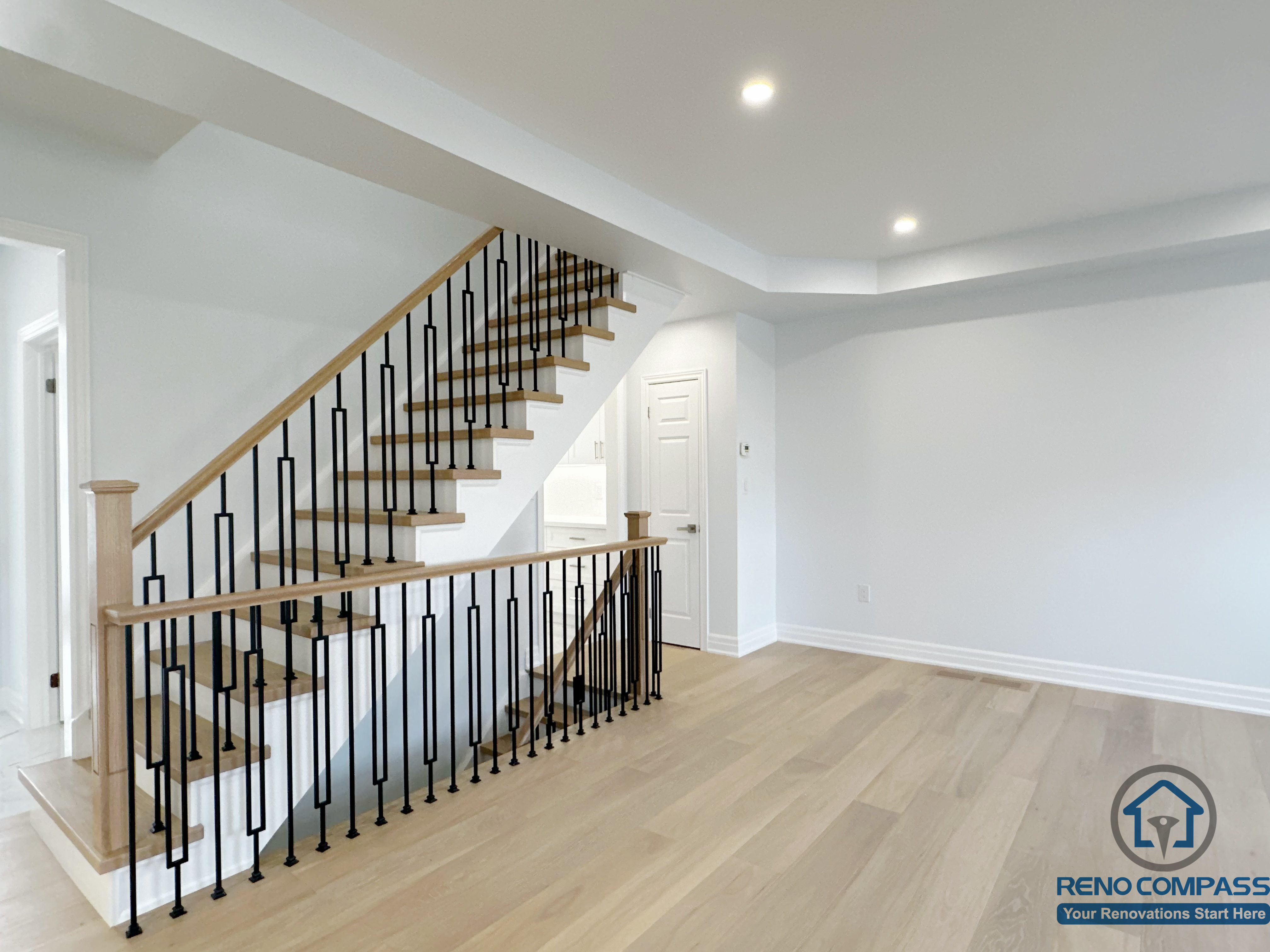 This image highlights the staircase and open main floor area in a Markham house renovation. The design features custom wood treads, black metal railings, and light-toned flooring, creating a clean visual connection between levels while improving openness, circulation, and overall spatial flow.