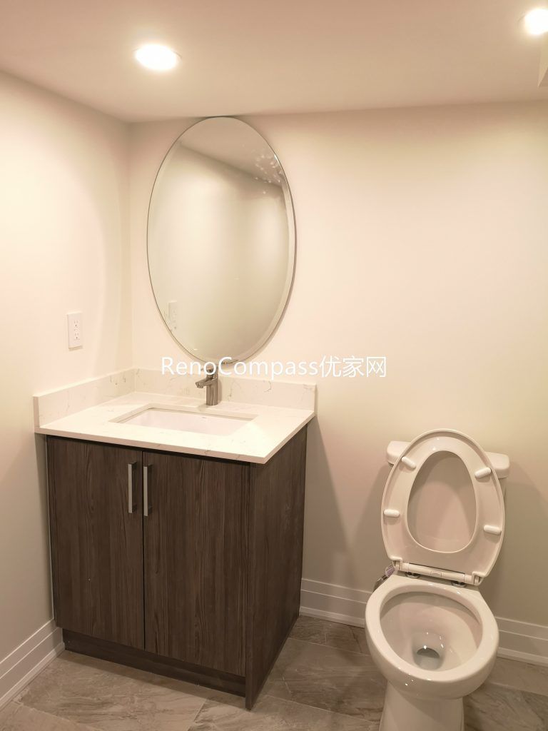 Newly renovated Richmond Hill basement bathroom featuring modern tile flooring, custom vanity cabinet, round mirror, and upgraded lighting. This basement renovation by Reno Compass Inc. enhances functionality, brightness, and modern comfort for everyday use.