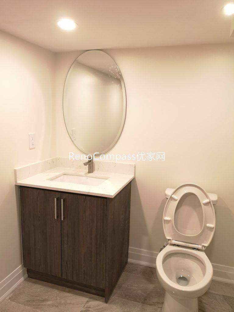 Newly renovated Richmond Hill basement bathroom featuring modern tile flooring, custom vanity cabinet, round mirror, and upgraded lighting. This basement renovation by Reno Compass Inc. enhances functionality, brightness, and modern comfort for everyday use.