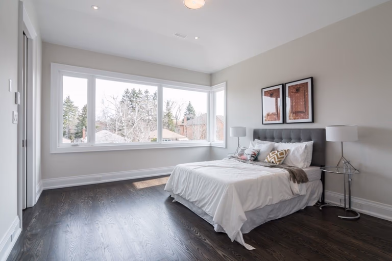 This elegant bedroom is part of a 4,500 sq ft modern home renovation in Toronto, designed to maximize natural light and comfort. Expansive corner windows brighten the space while dark hardwood flooring and soft neutral tones create a calm and contemporary atmosphere. The refined layout enhances both functionality and visual openness, reflecting the quality craftsmanship of a professional Toronto Renovation Company, Reno Compass Inc. This project highlights modern residential design tailored for luxury living.