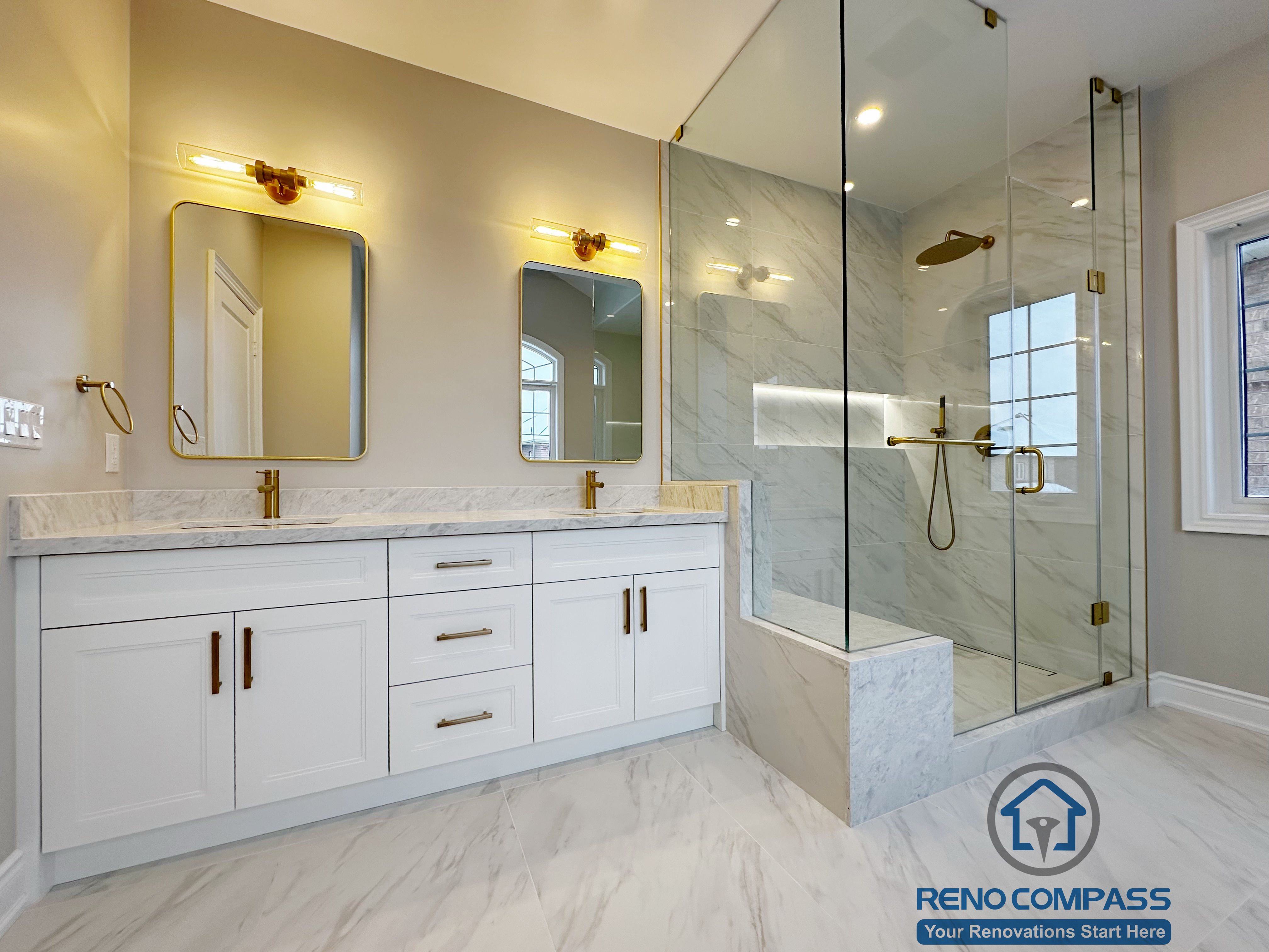 Spacious Vaughan primary bathroom renovation featuring a custom double vanity with quartz countertop, gold fixtures, backlit mirrors, and a frameless glass walk-in shower with marble-look tile walls. The layout balances functionality and luxury, completed by a trusted Toronto renovation company with attention to lighting, storage, and material coordination.