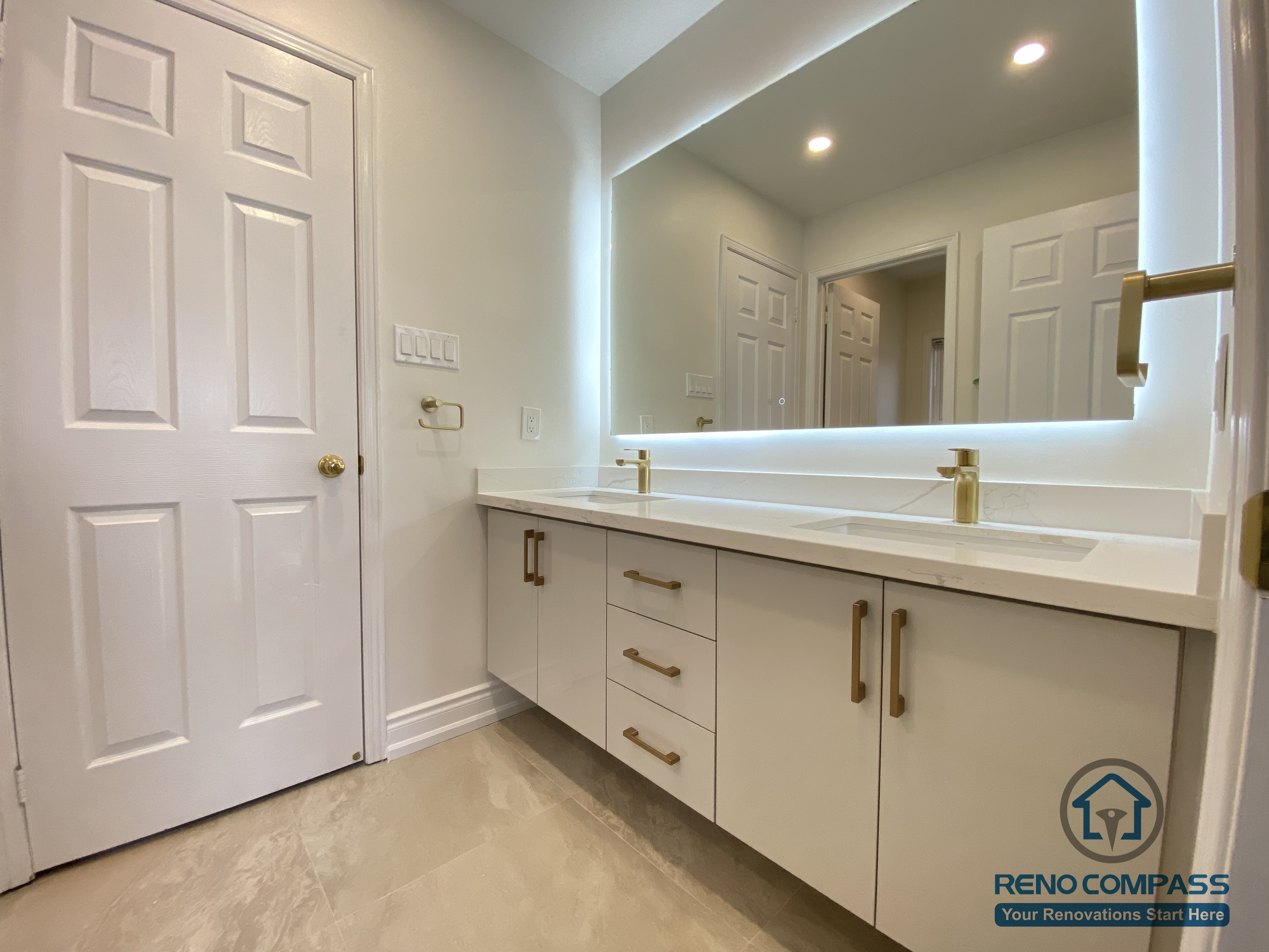 This Markham bathroom renovation highlights a custom double-sink vanity designed for shared daily use and long-term practicality. The clean-lined cabinetry is paired with quartz countertops, brushed brass hardware, and an oversized LED backlit mirror that enhances lighting and visual depth. Neutral floor tiles and a streamlined layout improve circulation while maintaining a calm, modern aesthetic. Completed by an experienced Toronto renovation company, this bathroom upgrade emphasizes functionality, storage efficiency, and timeless residential design.